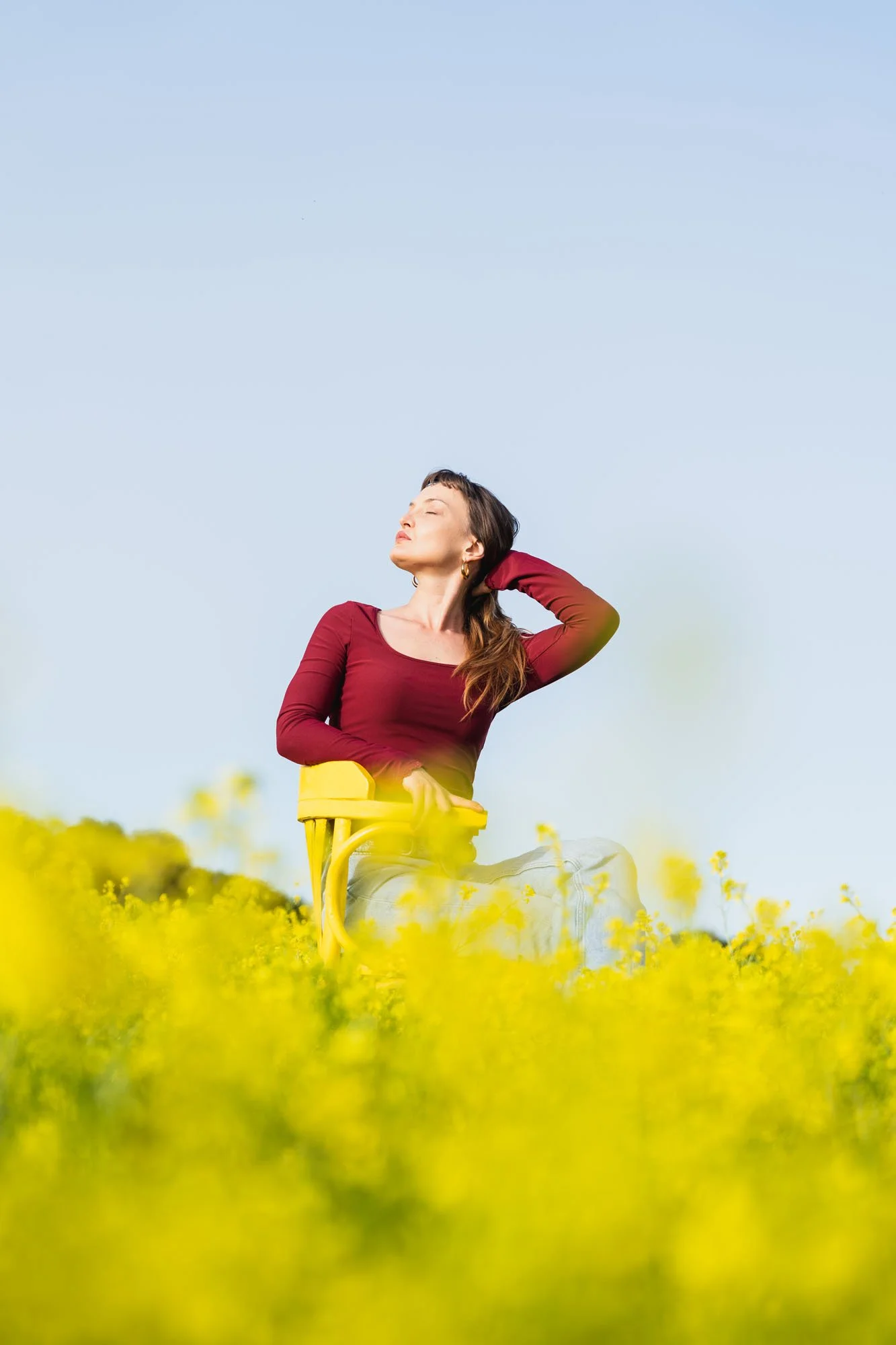Mujer sentada en una silla amarilla en un campo de flores amarillas, con ojos cerrados y una expresión de calma.