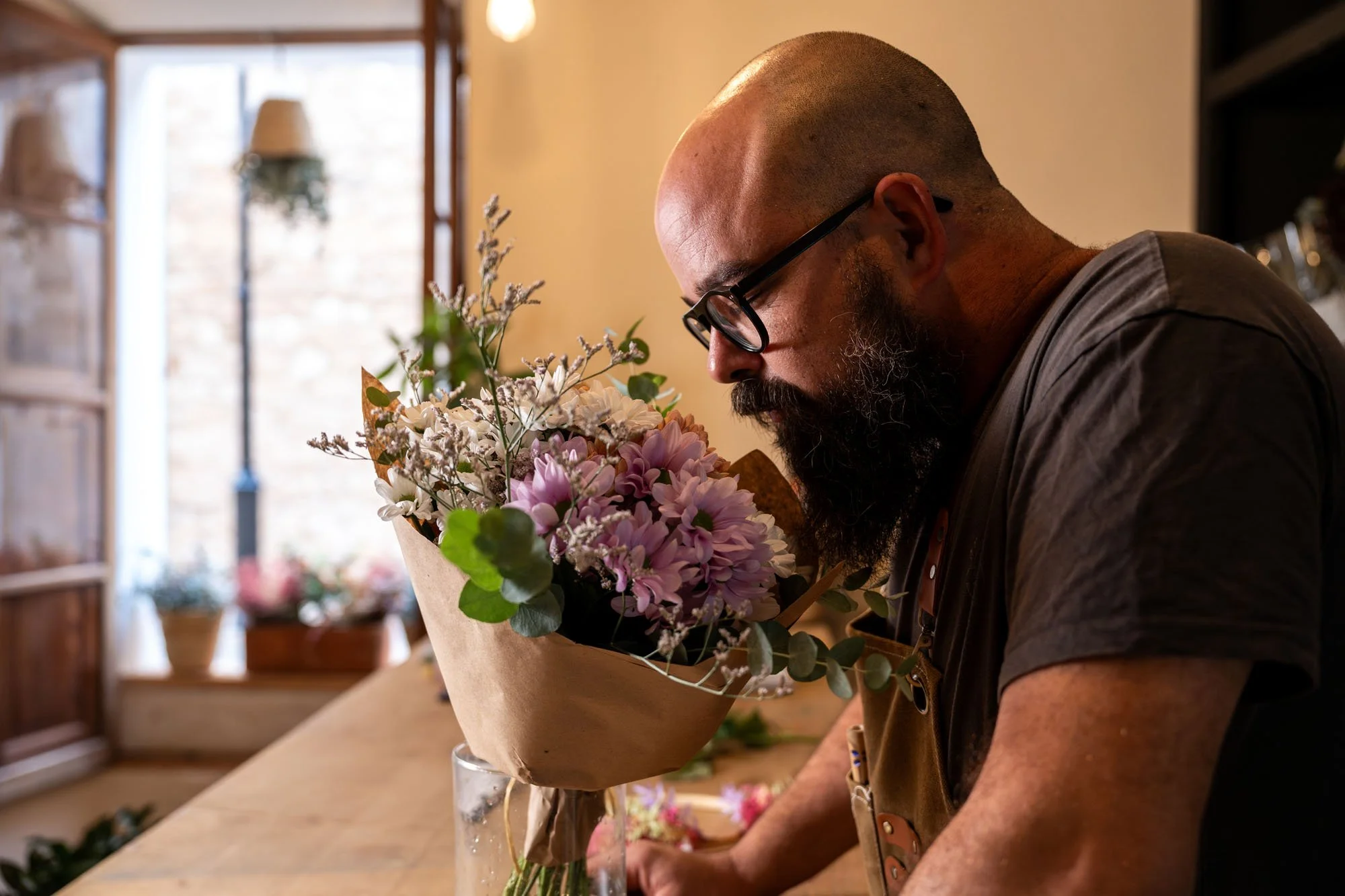 Hombre con barba y gafas sosteniendo un ramo de flores en una tienda de flores.
