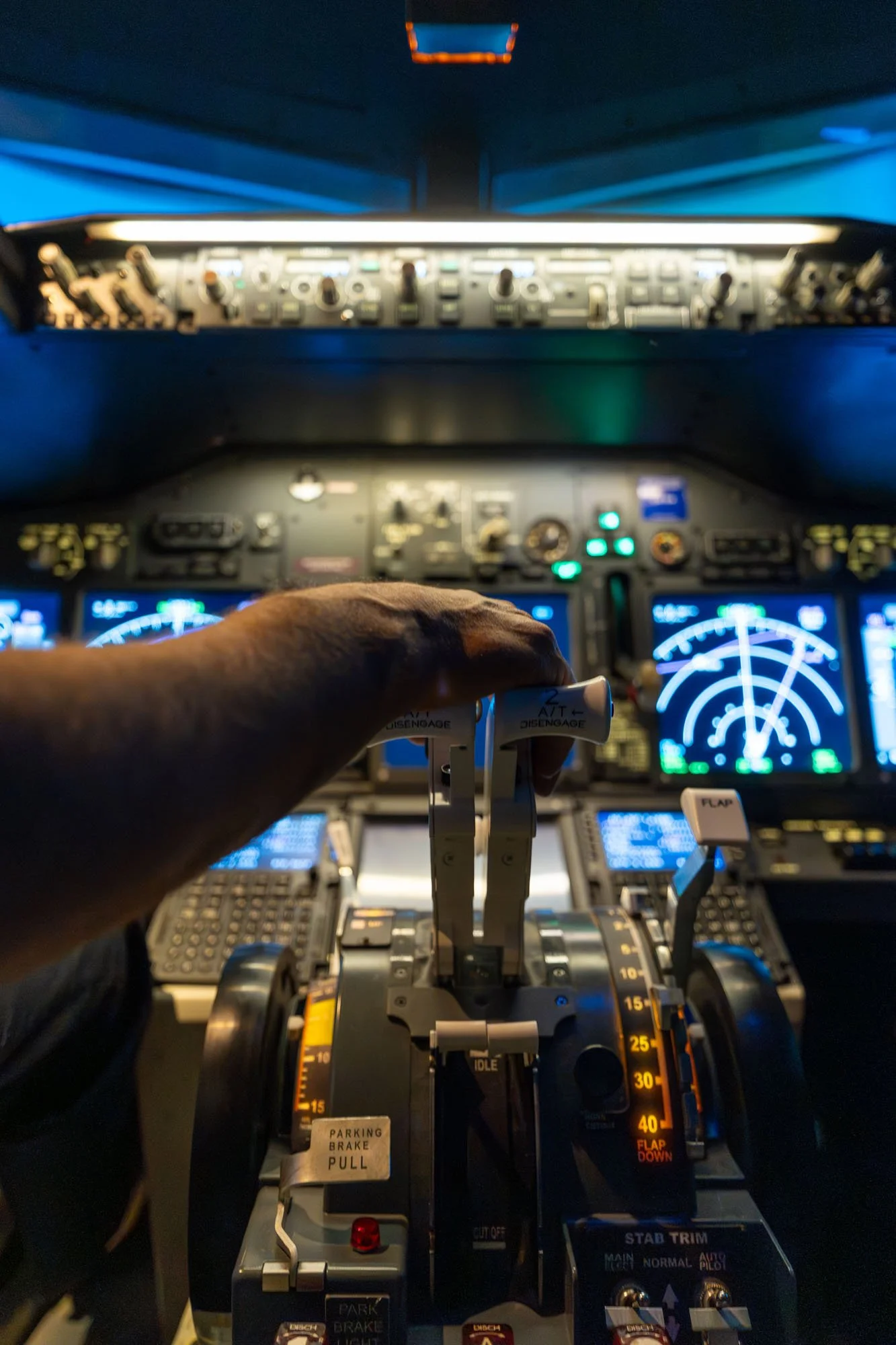Vista del panel de instrumentos y controles de una cabina de avión, incluyendo botones, perillas y pantallas con instrumentos de vuelo, con una mano ajustando un control.