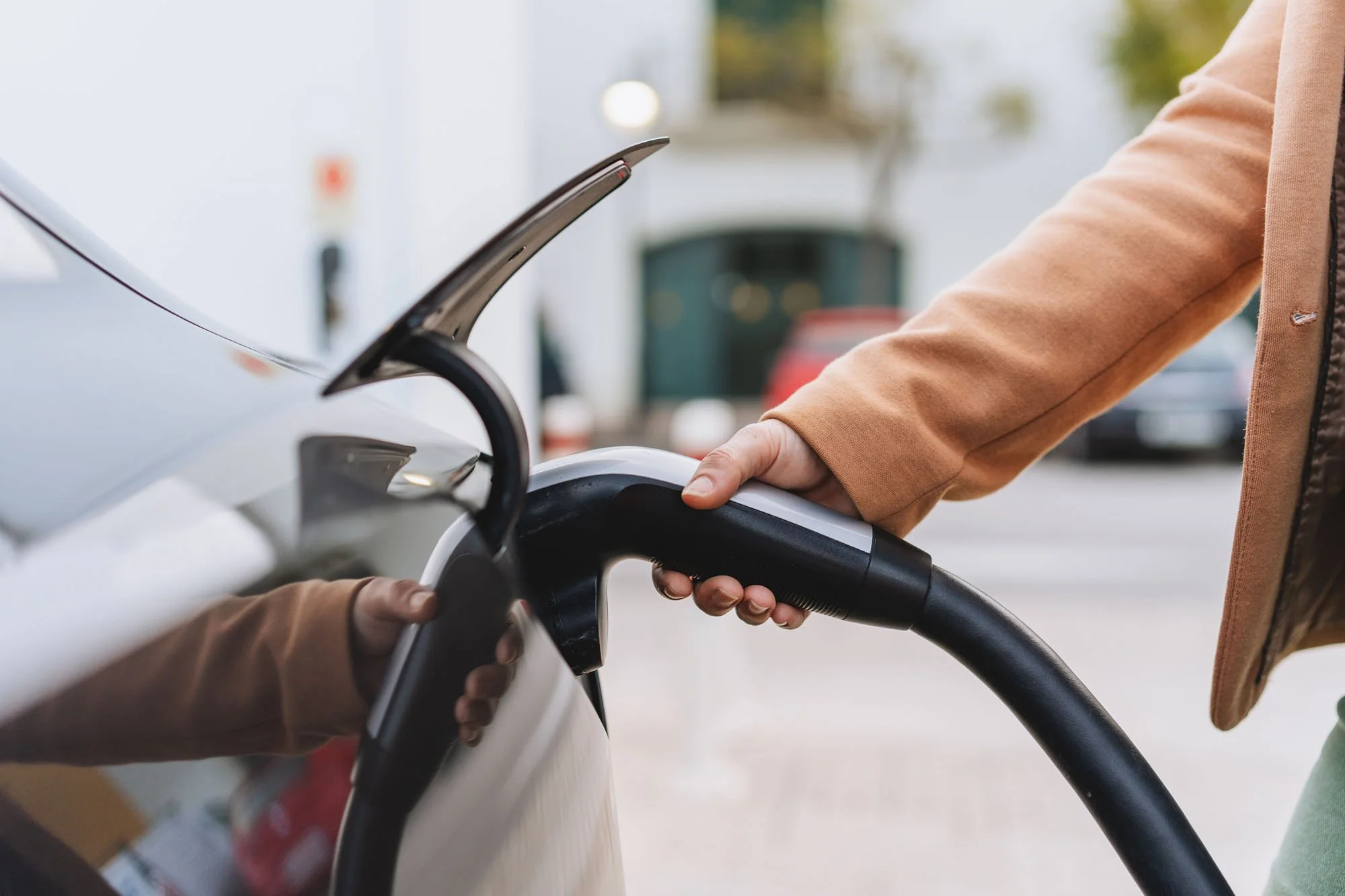 Persona cargando un coche eléctrico conectándolo a un cargador portátil.
