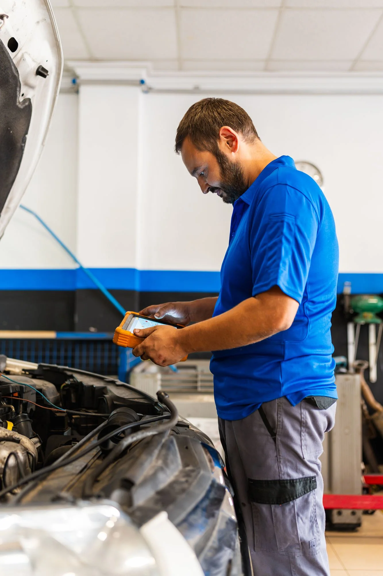Un técnico en mecánica revisa el motor de un automóvil con una herramienta de diagnóstico en una taller mecánico.