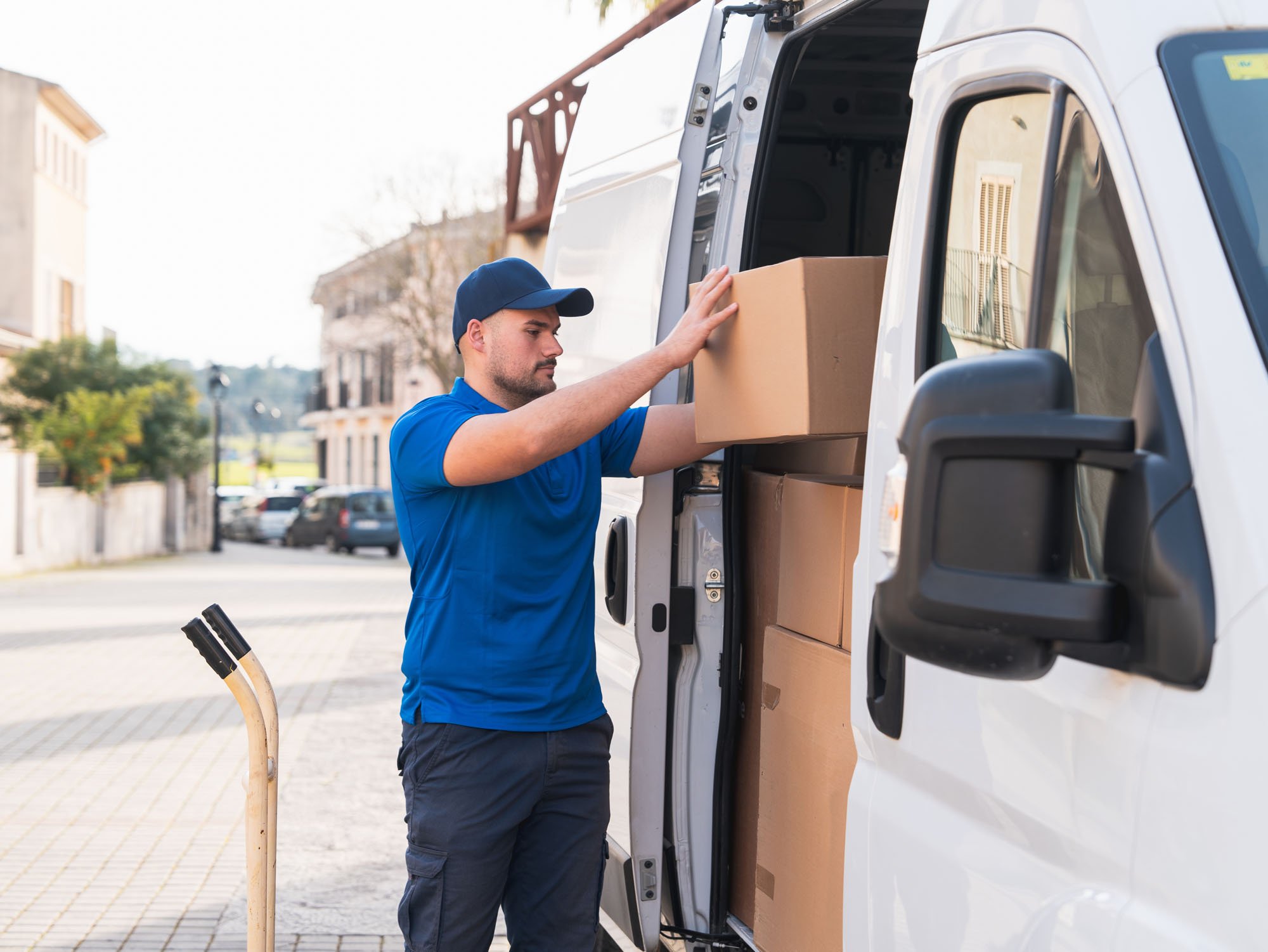 Hombre colocando cajas en una camioneta de reparto en una calle urbana.
