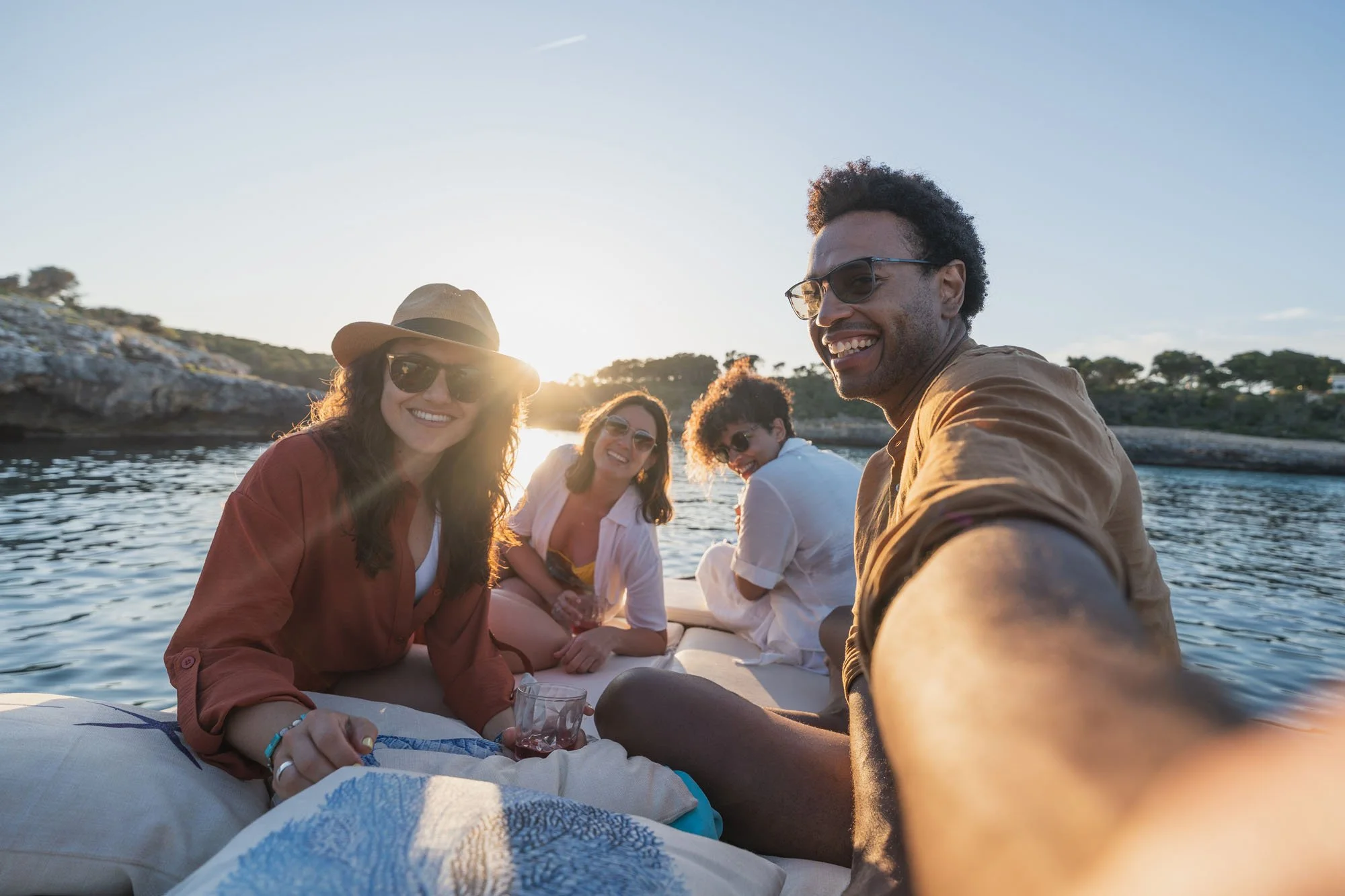 Grupo de amigos en barco en un lago o río durante el atardecer, sonriendo y disfrutando del momento.