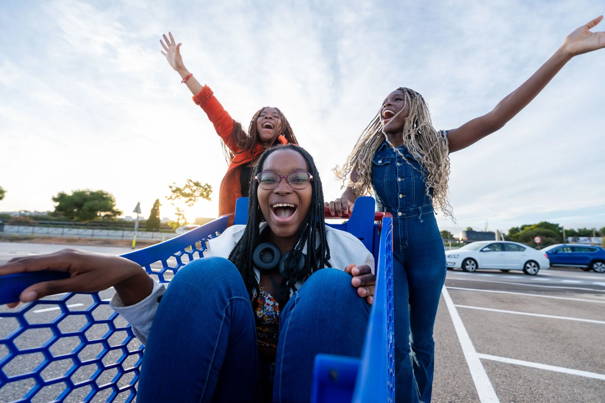 Tres mujeres felices en una plaza, una en una silla de compras con las piernas levantadas, las otras dos de pie, con los brazos en alto, celebrando.