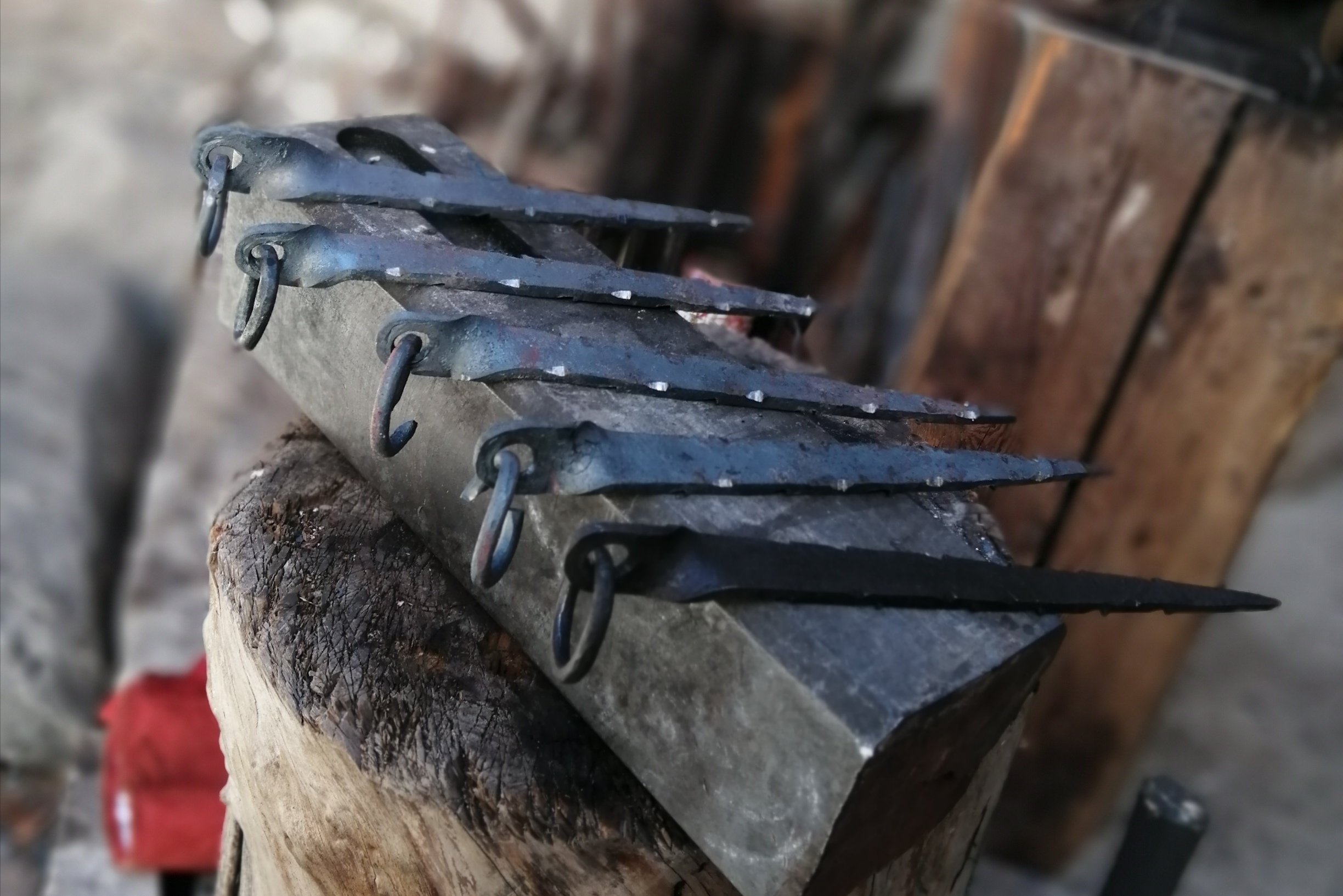Des pitons à glace en fer forgé posés sur une enclume, avec un arrière-plan de bois assemblé.