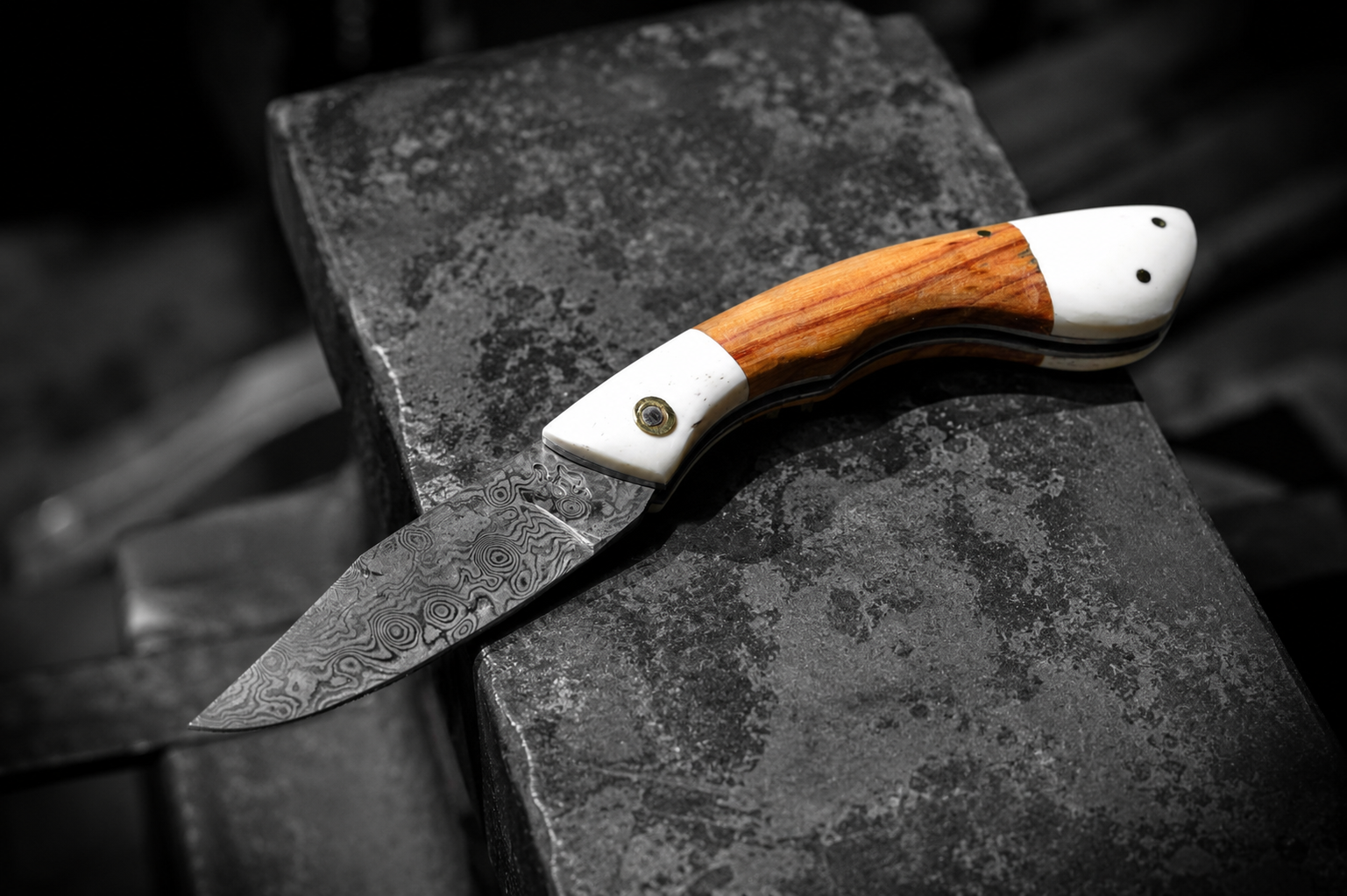 Un couteau avec une lame en damas et un manche en bois et en ivoire, posé sur une surface de pierre sombre.