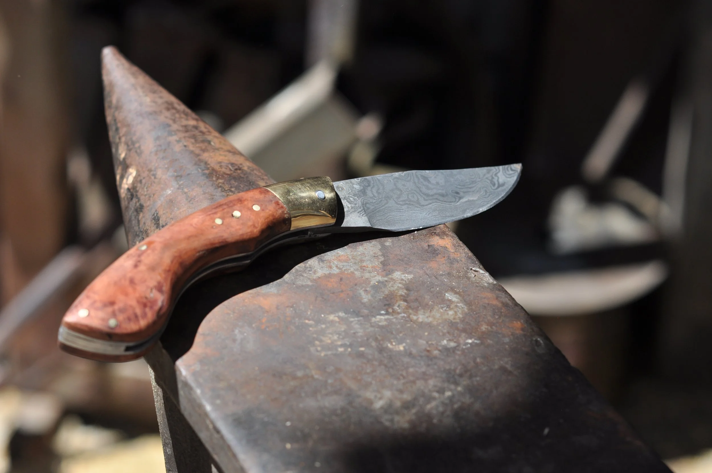 Un couteau artisanal avec une lame en acier à motifs et une poignée en bois repose sur une surface en métal rouillée.