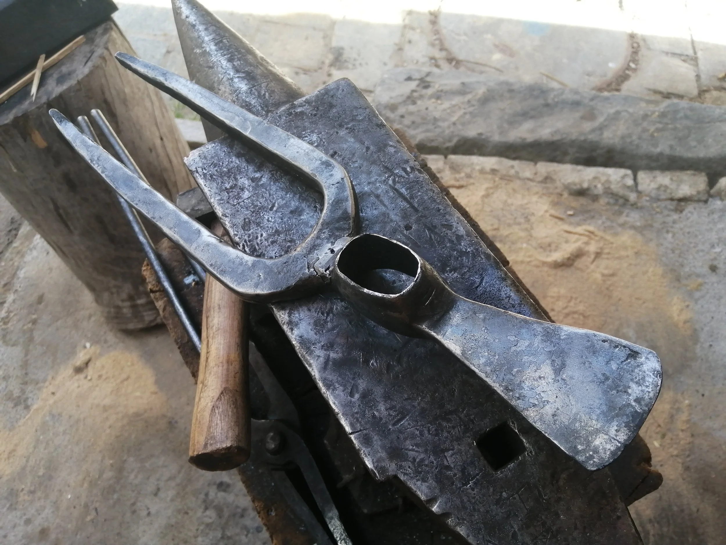 Outils de jardinage ancien forgé posé sur une enclume, sur une souche de bois dans un atelier de forge.