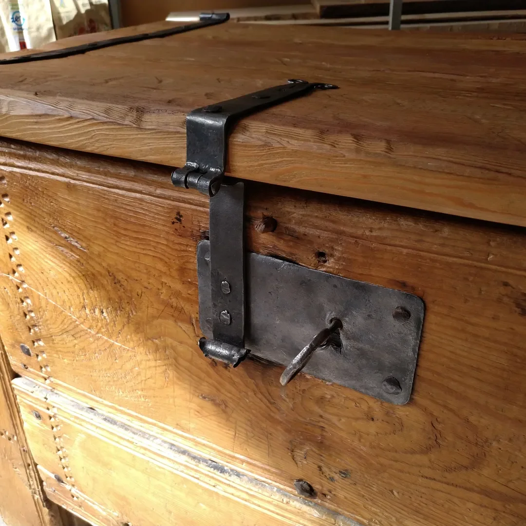 Ancien coffre en bois avec verrou en métal forgé, clé suspendue dans une serrure.