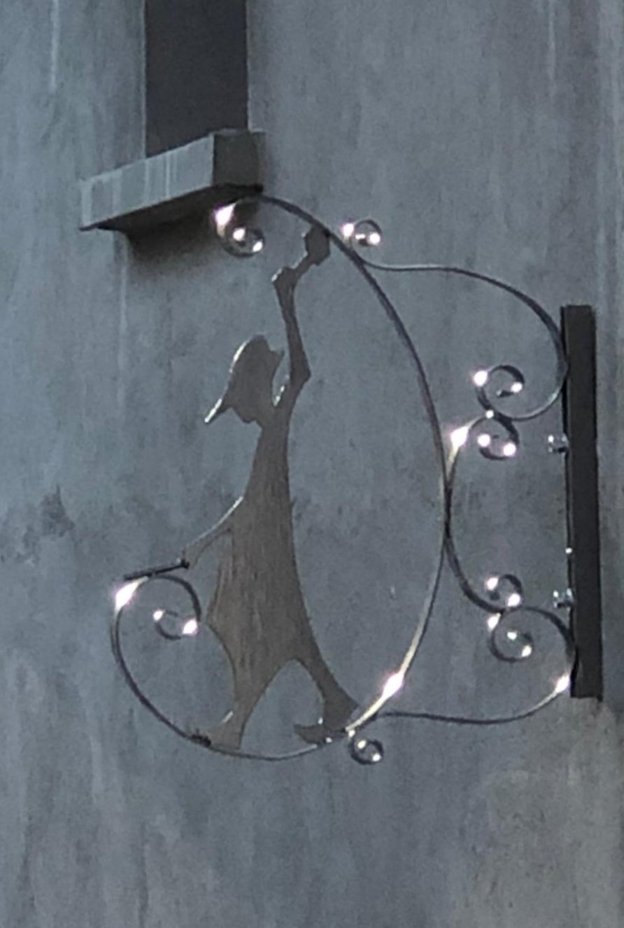 Décor en métal représentant une silhouette de forgerons avec des courbes décoratives, fixé sur un mur en béton.