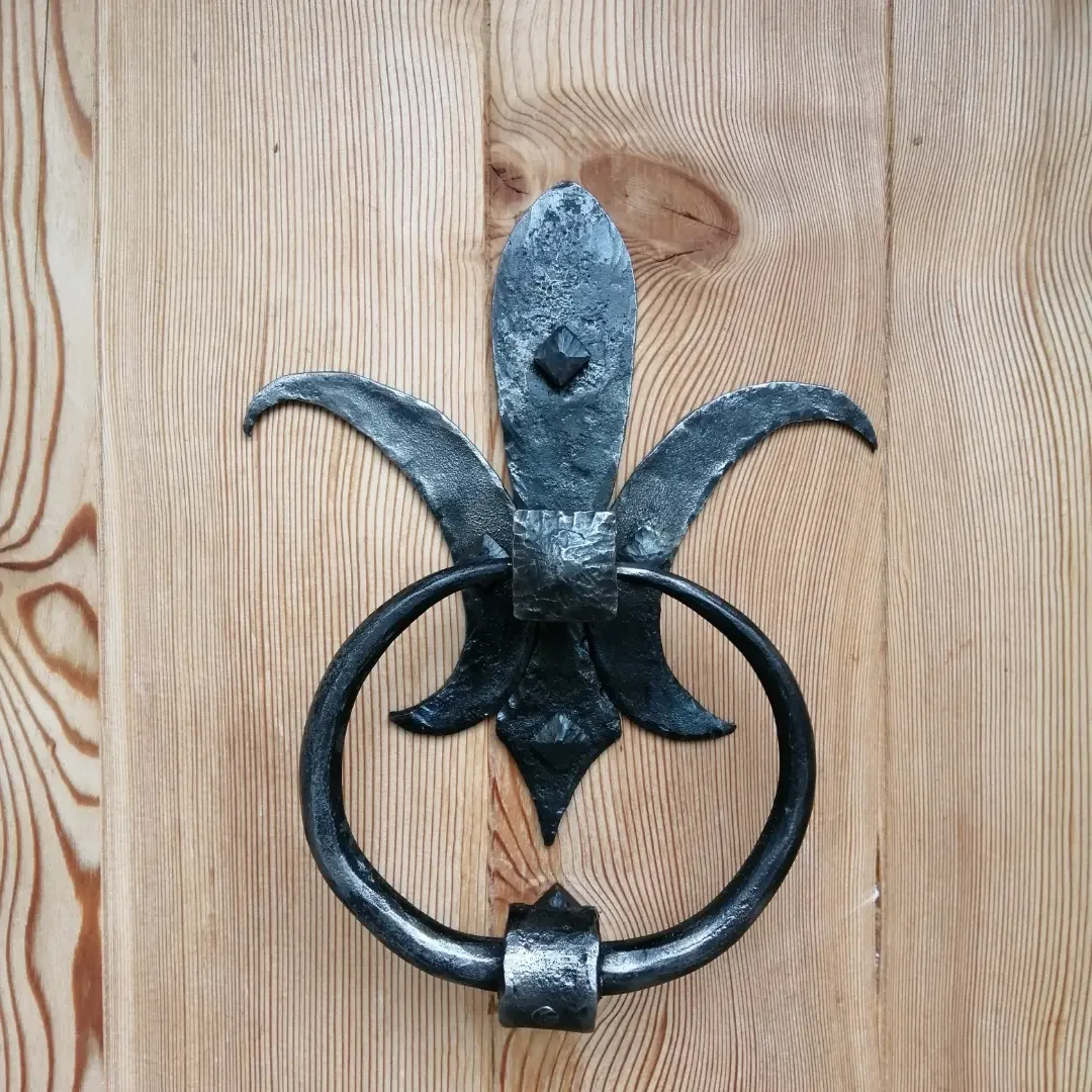 heurtoir de porte en fer forgé de style fleur de lys fixée sur une surface en bois.