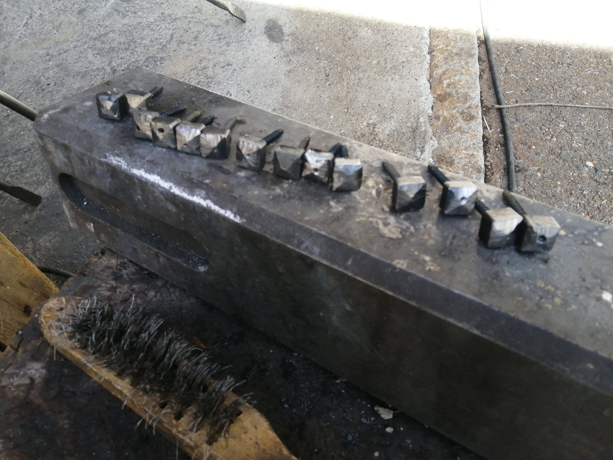 Une pièce métallique avec des clous forgés tête de diamant posés sur une enclume.