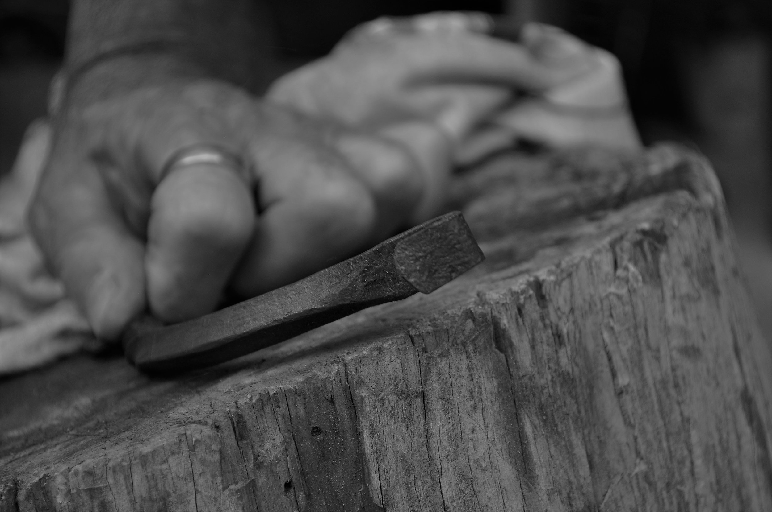 Une main qui tient une pièce en acier forgé sur une souche en bois.