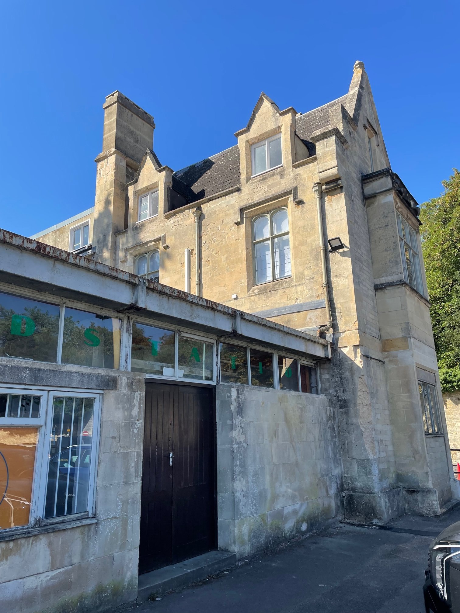 A multi-story stone building with gothic style pointed gables and large windows, with a modern storefront at the ground level featuring glass windows and a wooden door, set against a clear blue sky.