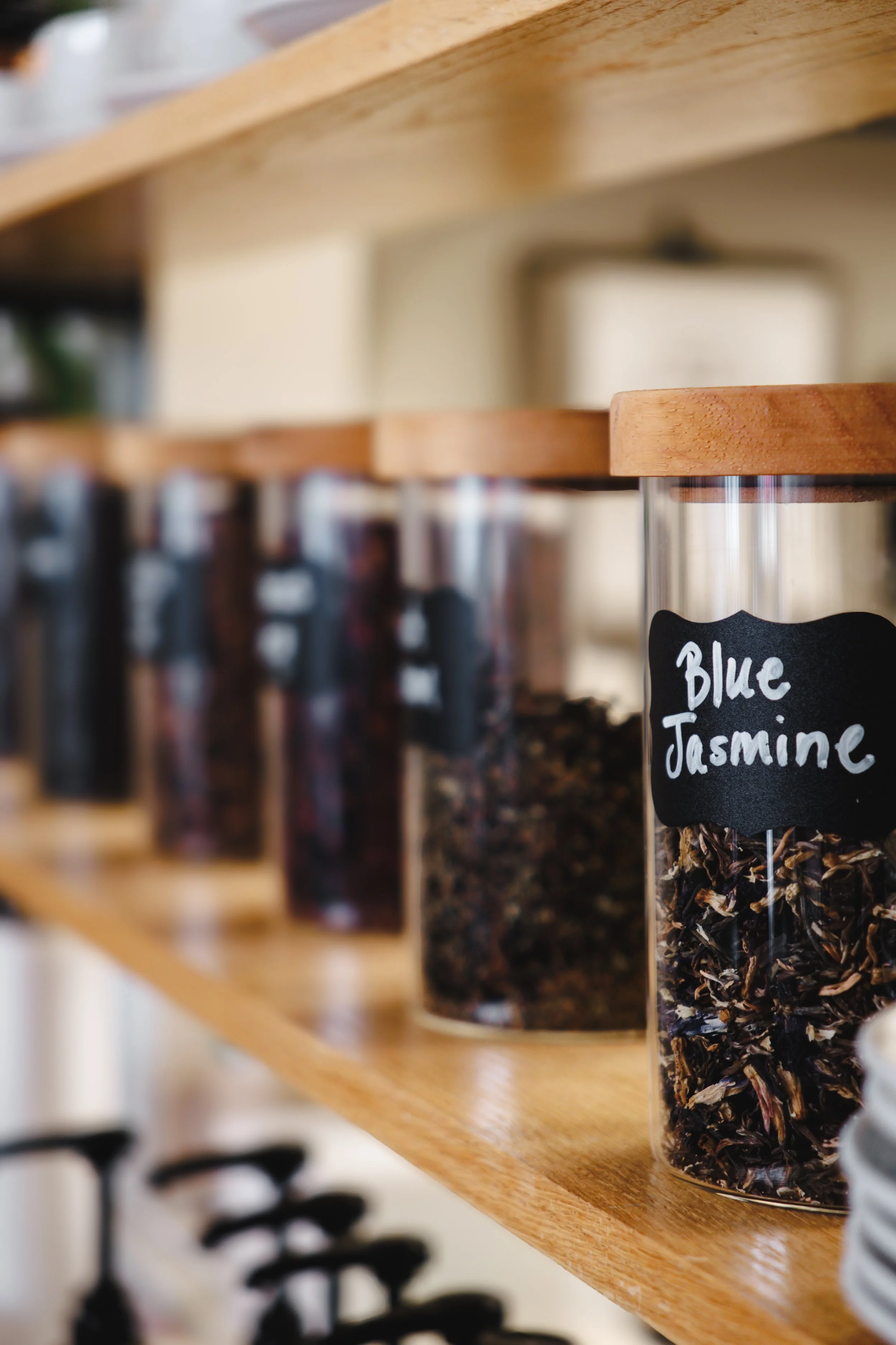 Clear glass jar filled with dried blue jasmine flowers on a wooden shelf, labeled with a chalkboard-style sign.