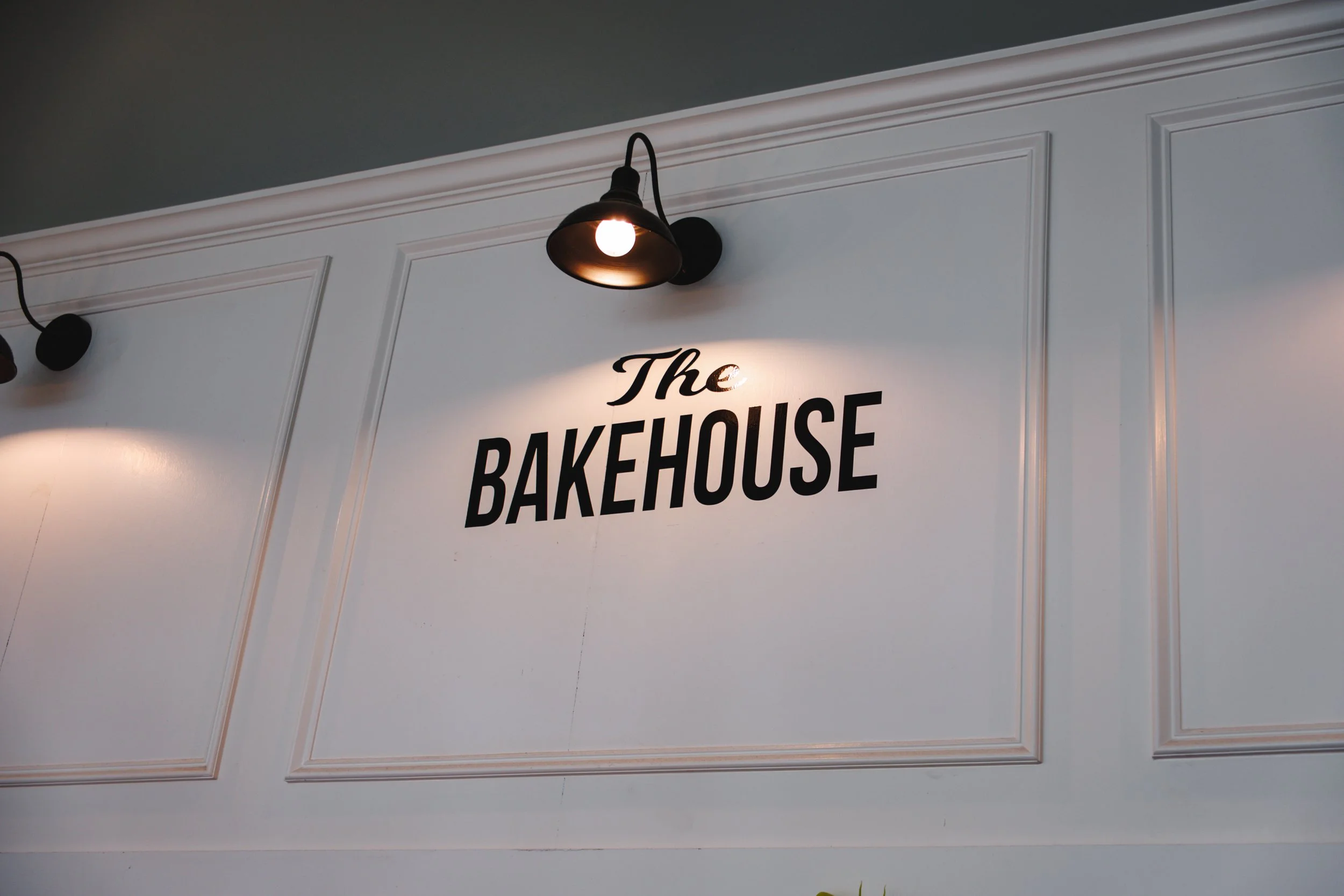 Interior wall with the sign 'The BAKEHOUSE' illuminated by a black wall-mounted light fixture.