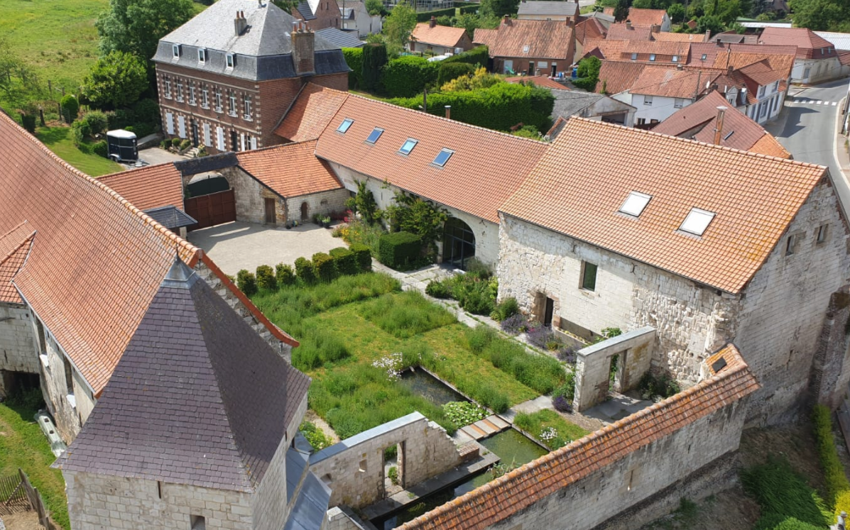 Aerial view of a European village with historic stone buildings, lush gardens, and red-tiled roofs.