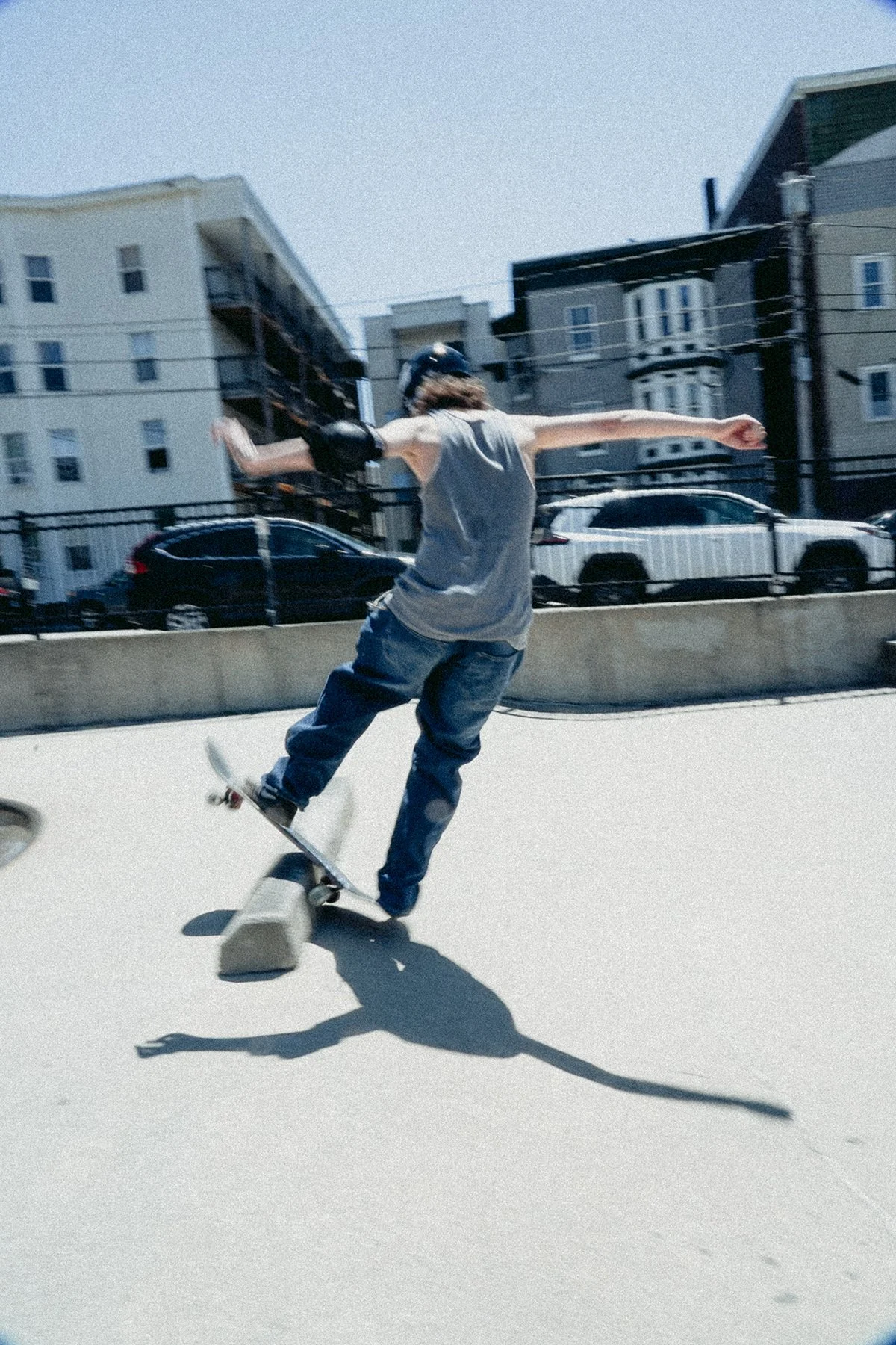 grainy colored film shot of a person skating; their back trucks are just touching a curb, and the nose is up.