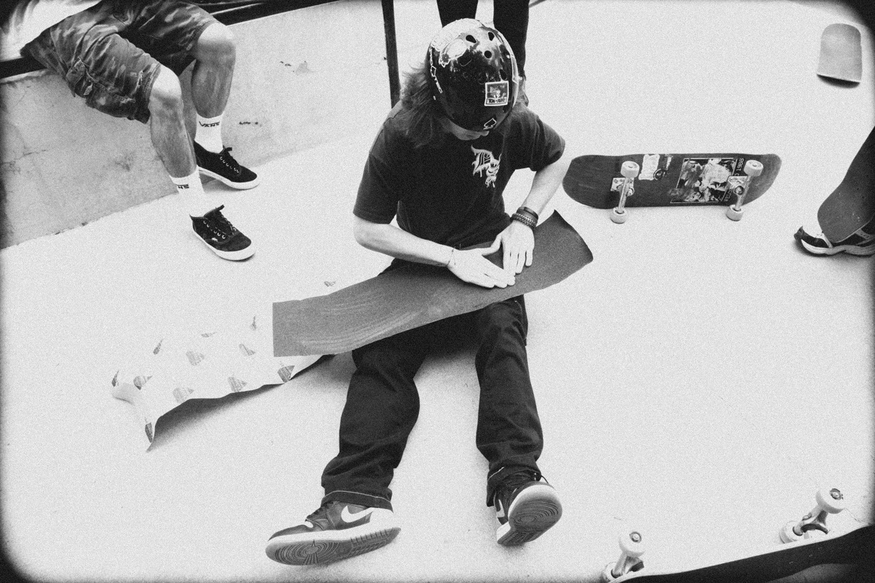 black and white film shot of a young person putting griptape on a skateboard.