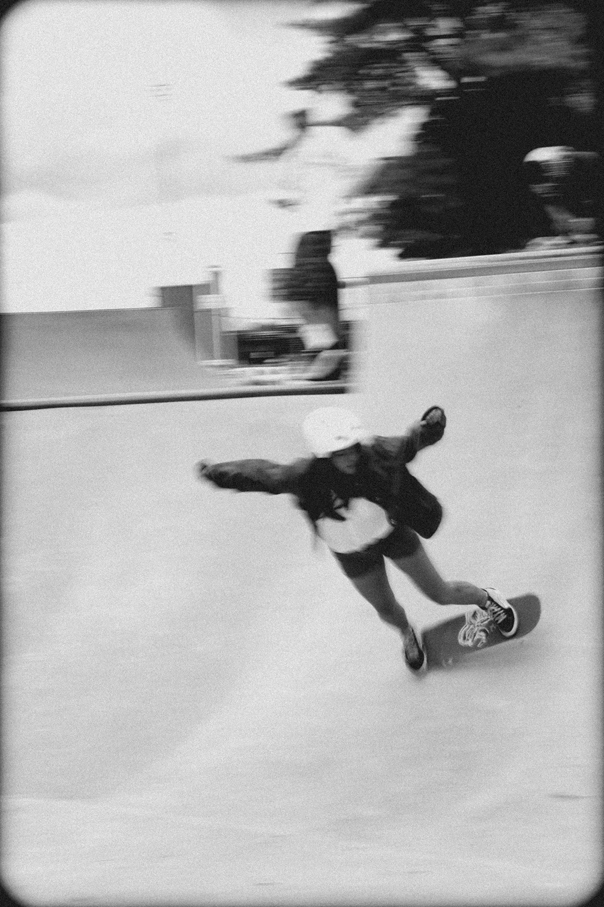 black and white grainy photo of someone who looks like they are carving on a skateboard. its blurry from movement.