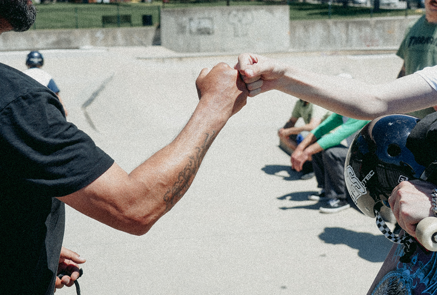 Close up grainy shot of two hands fistbumping, background is a skatepark.