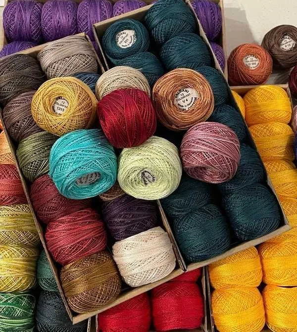 Colorful skeins of yarn in various colors such as purple, beige, teal, red, pink, yellow, orange, and soft green, arranged in boxes for knitting or crocheting.