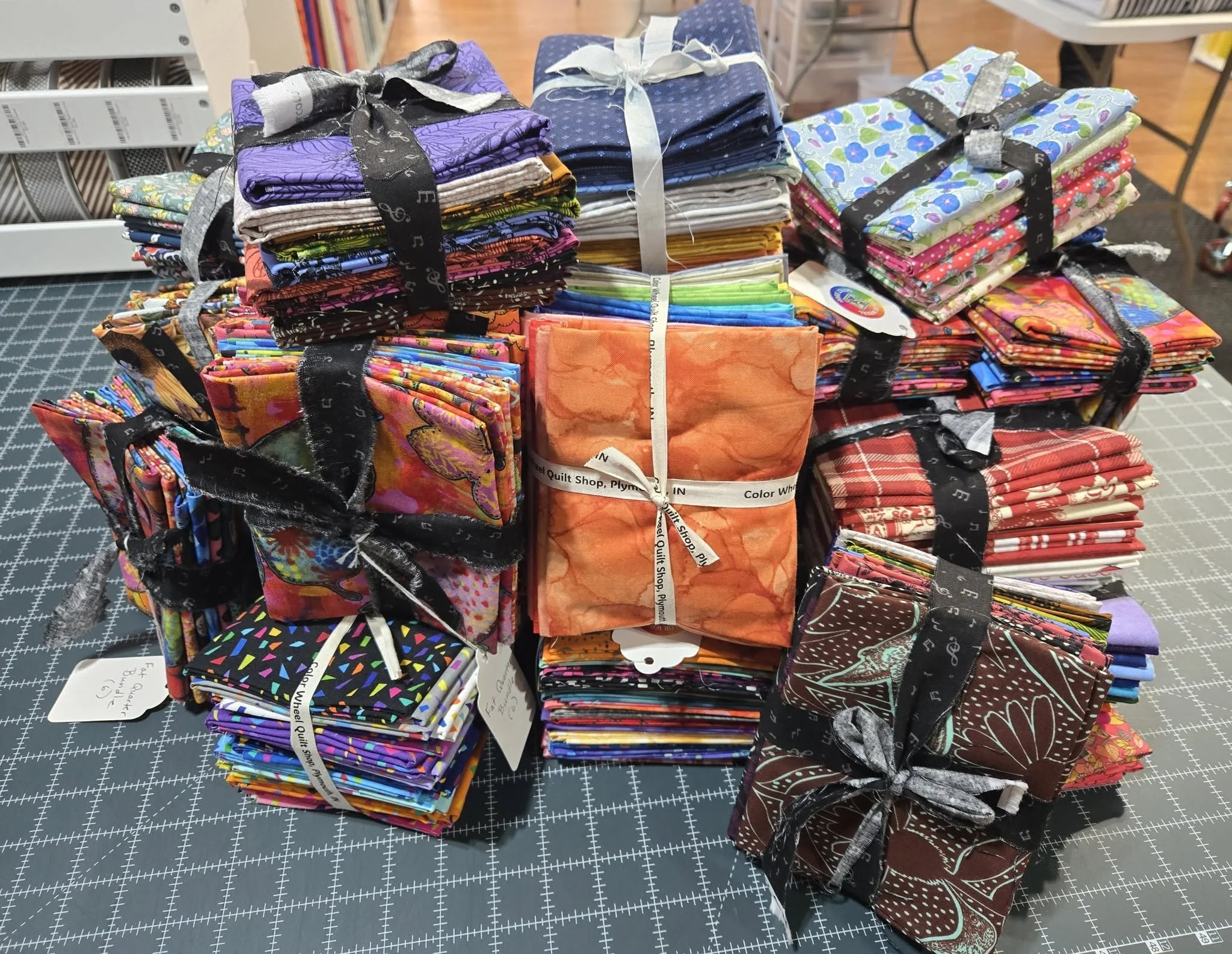 Several stacks of colorful fabric squares, tied with black ribbons, on a cutting mat at a quilt shop.