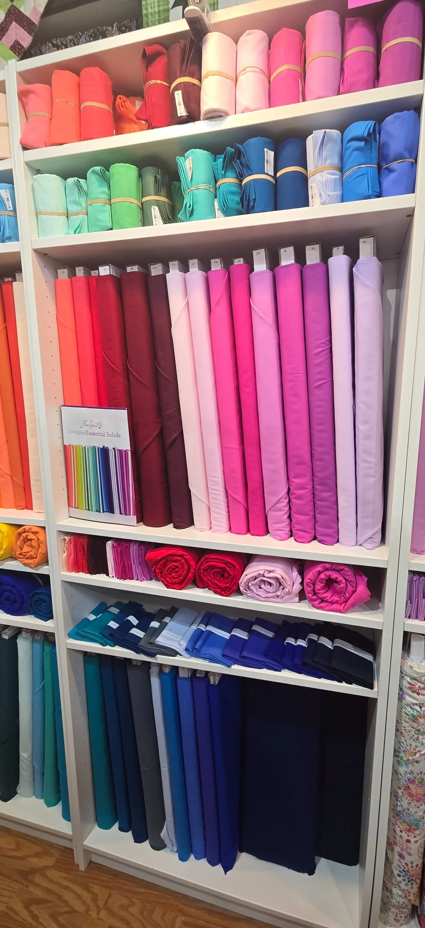 Shelves of colorful fabrics arranged by color, including shades of red, pink, purple, blue, green, and black, in a fabric or craft store.