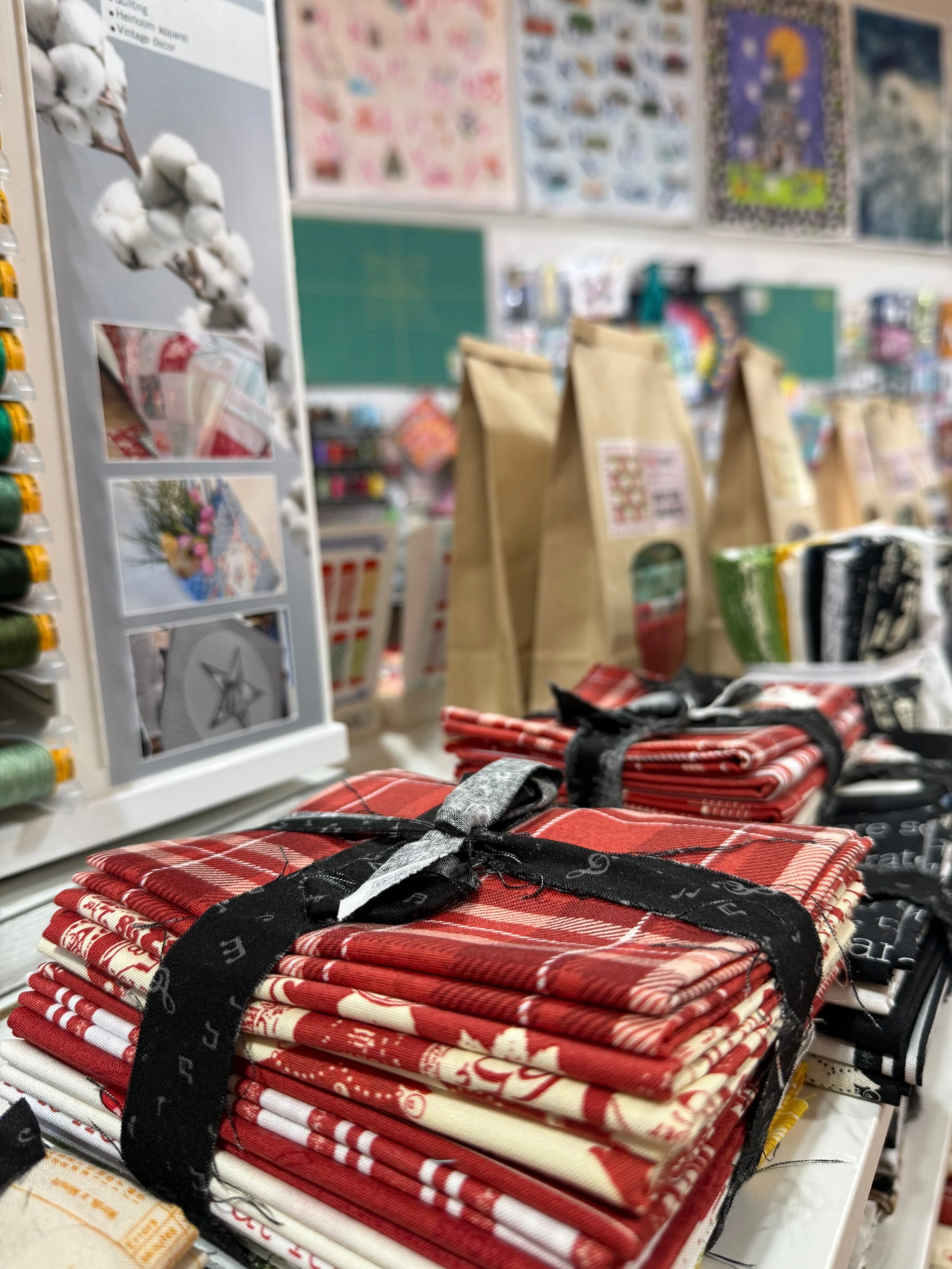 A display of folded red, white, and cream plaid fabric items tied with black ribbons in a store. In the background, shelves with various products and posters are visible.