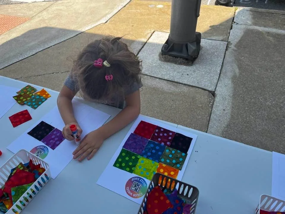 Child working on a color matching activity with fabric swatches and glue, outdoors at a table.