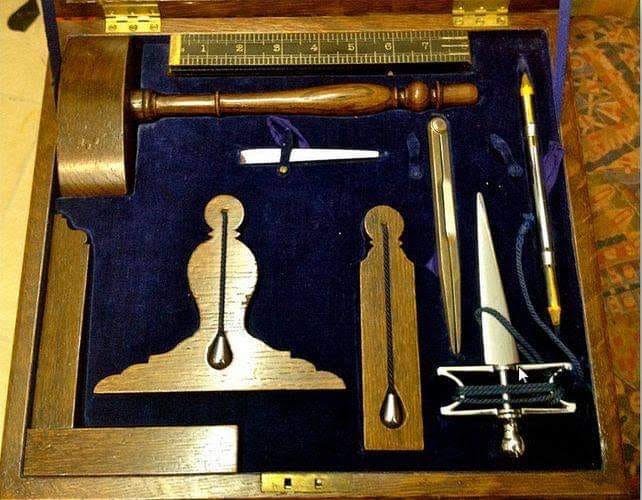 Masonic working tools arranged together, including a gauge, gavel, square, level, and plumb.