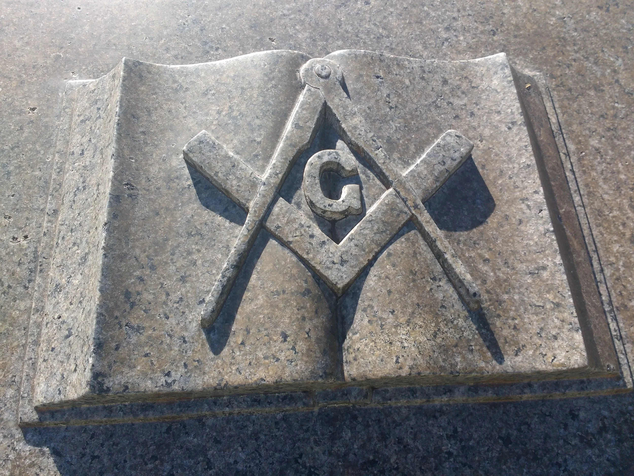 Carved Granite Square And Compasses on a Bible, sourced at -https://www.photos-public-domain.com/2017/06/22/free-mason-symbol-granite/#google_vignette