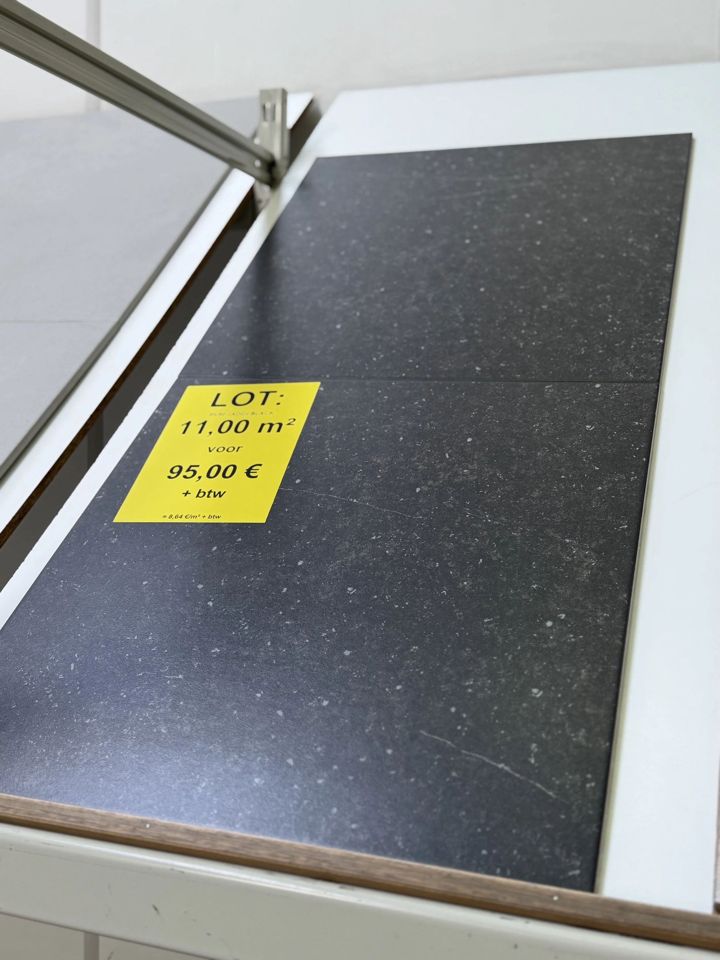 Donkere tegelvloer met een gele prijskaartje erop dat 11,00 m² kost voor 95,00 €, inclusief btw.