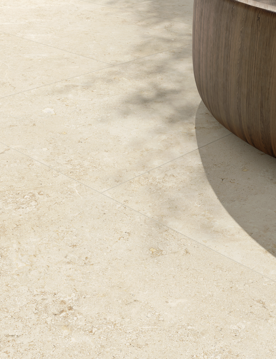 Een close-up van een beige stenen vloer met een ronde houten structuur aan de rechterkant die een schaduw werpt.