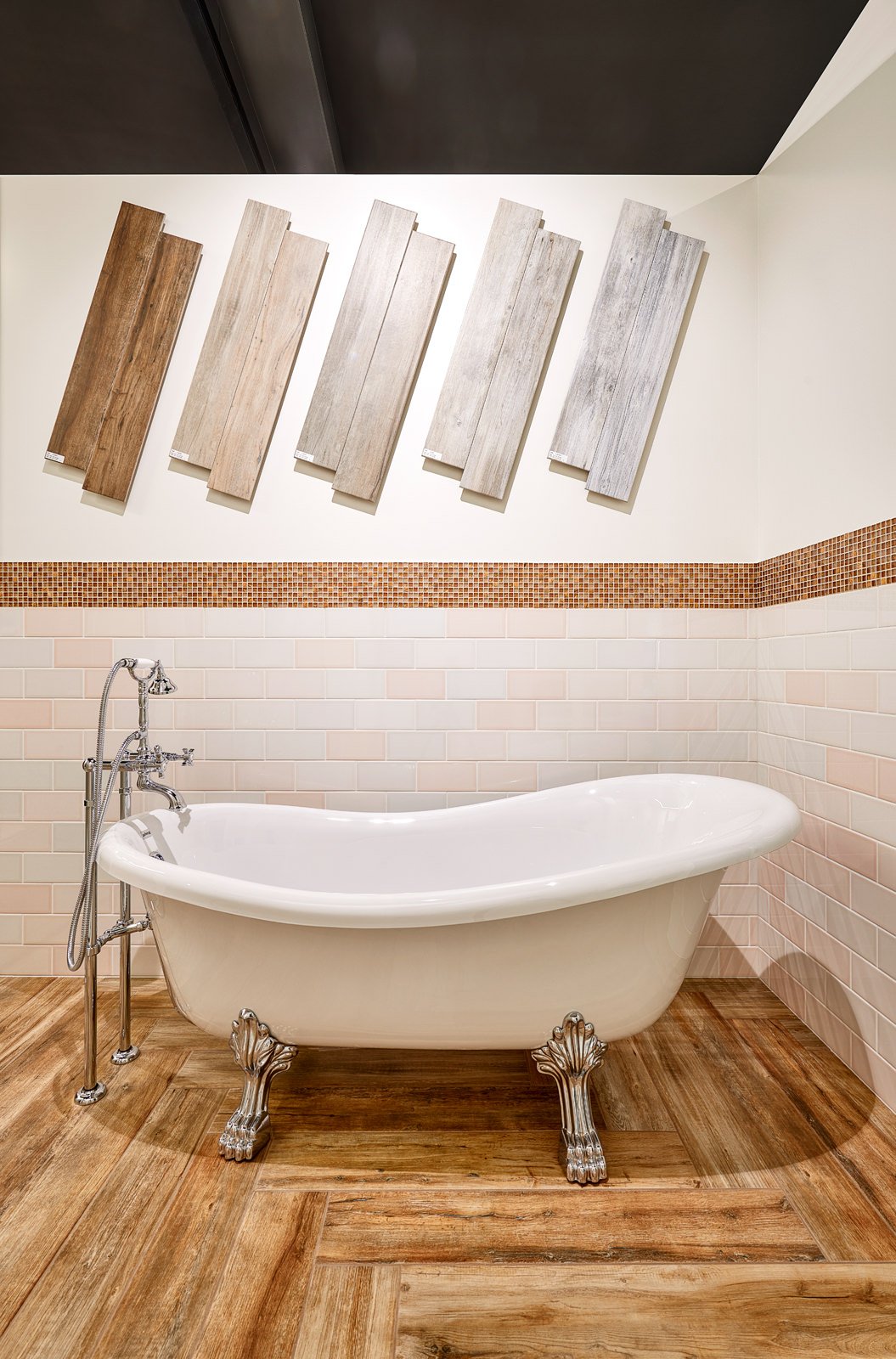 Een witte, vintage badkuip met sierlijke pootjes in een badkamer met houten vloer, betegelde muur en een ton-sur-ton kleurenthema, houtstalen aan de muur hangen erboven.
