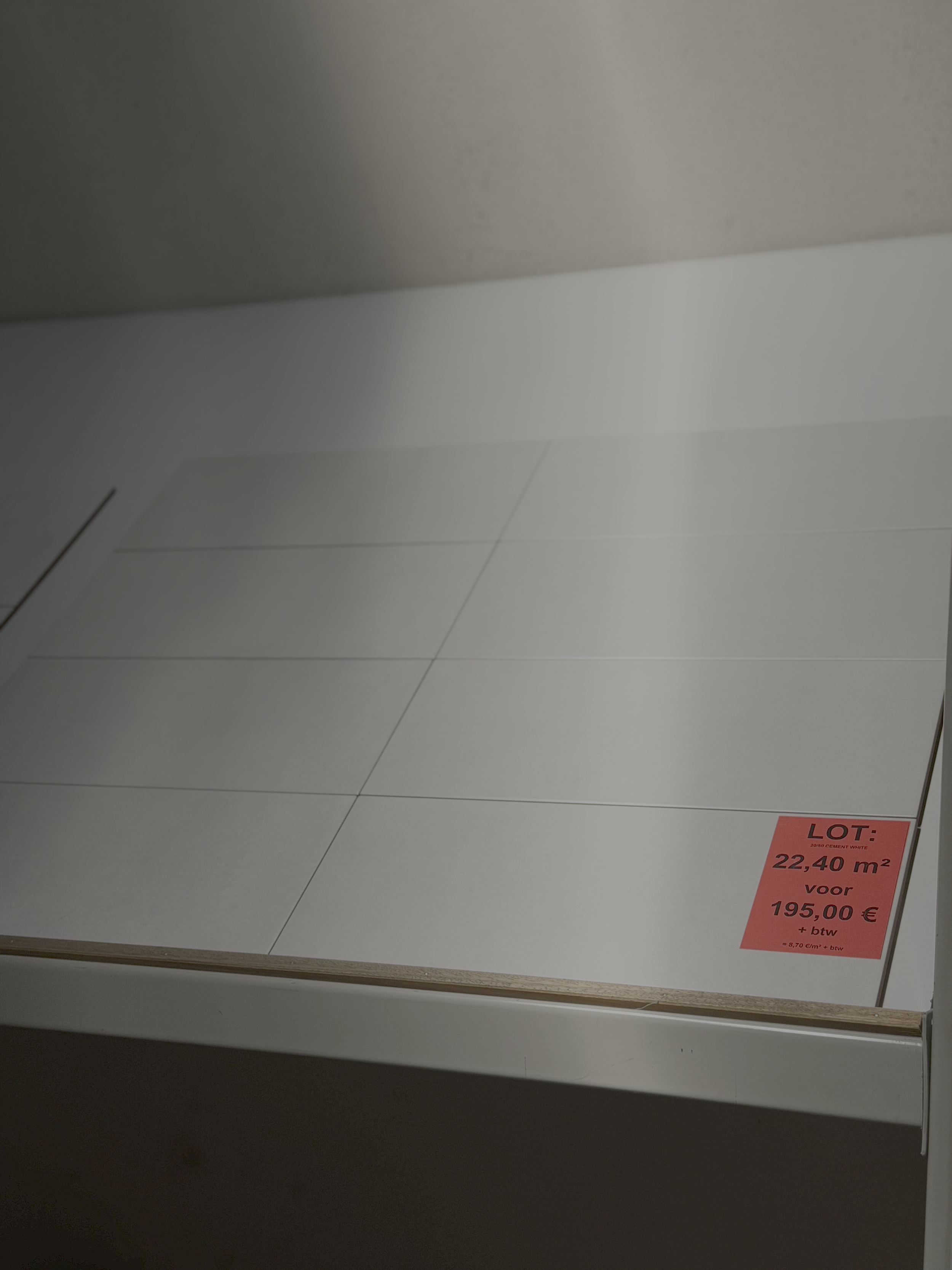 Witte vloertegels met een rood prijskaartje dat aangeeft dat de vloer 22,40 m² kost voor 195,00 € inclusief btw.