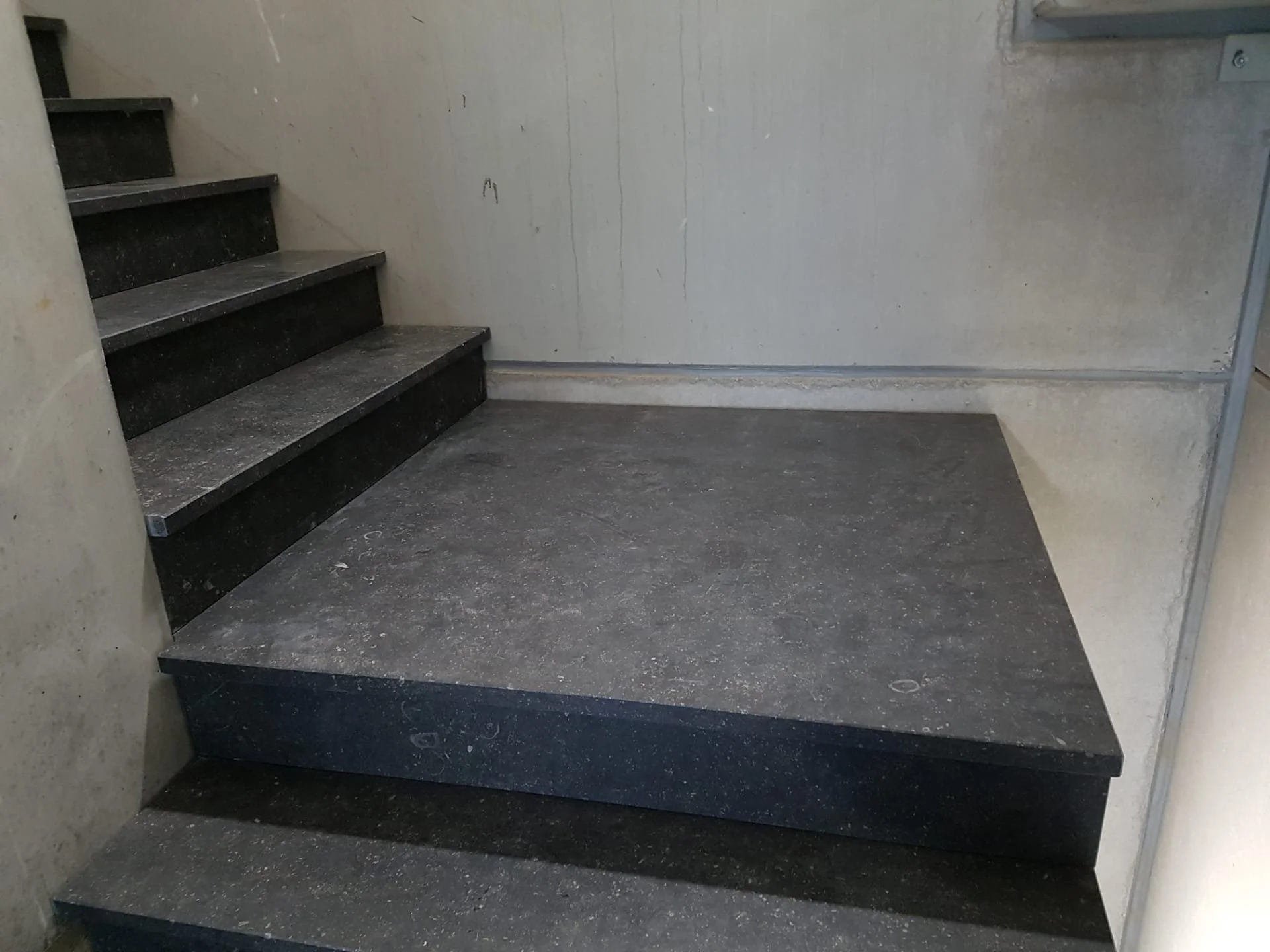 Donkere trappen naar de verdieping met een grijze wand en vloer.
