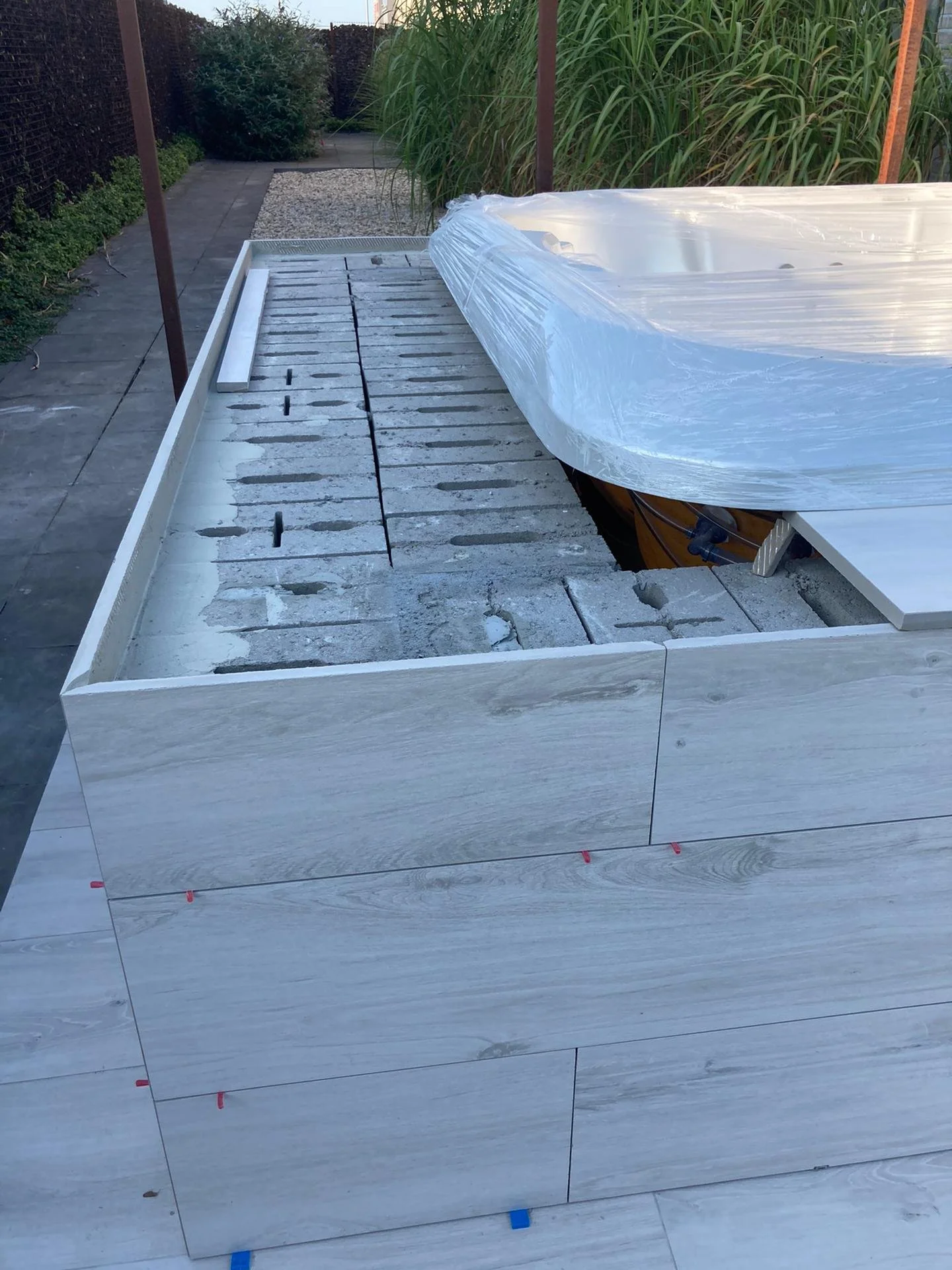 Bouw van een buitenmuur met wit marmer tegels, met gereedschap en bouwmaterialen op de werkplek, omstreeks eind van de middag.