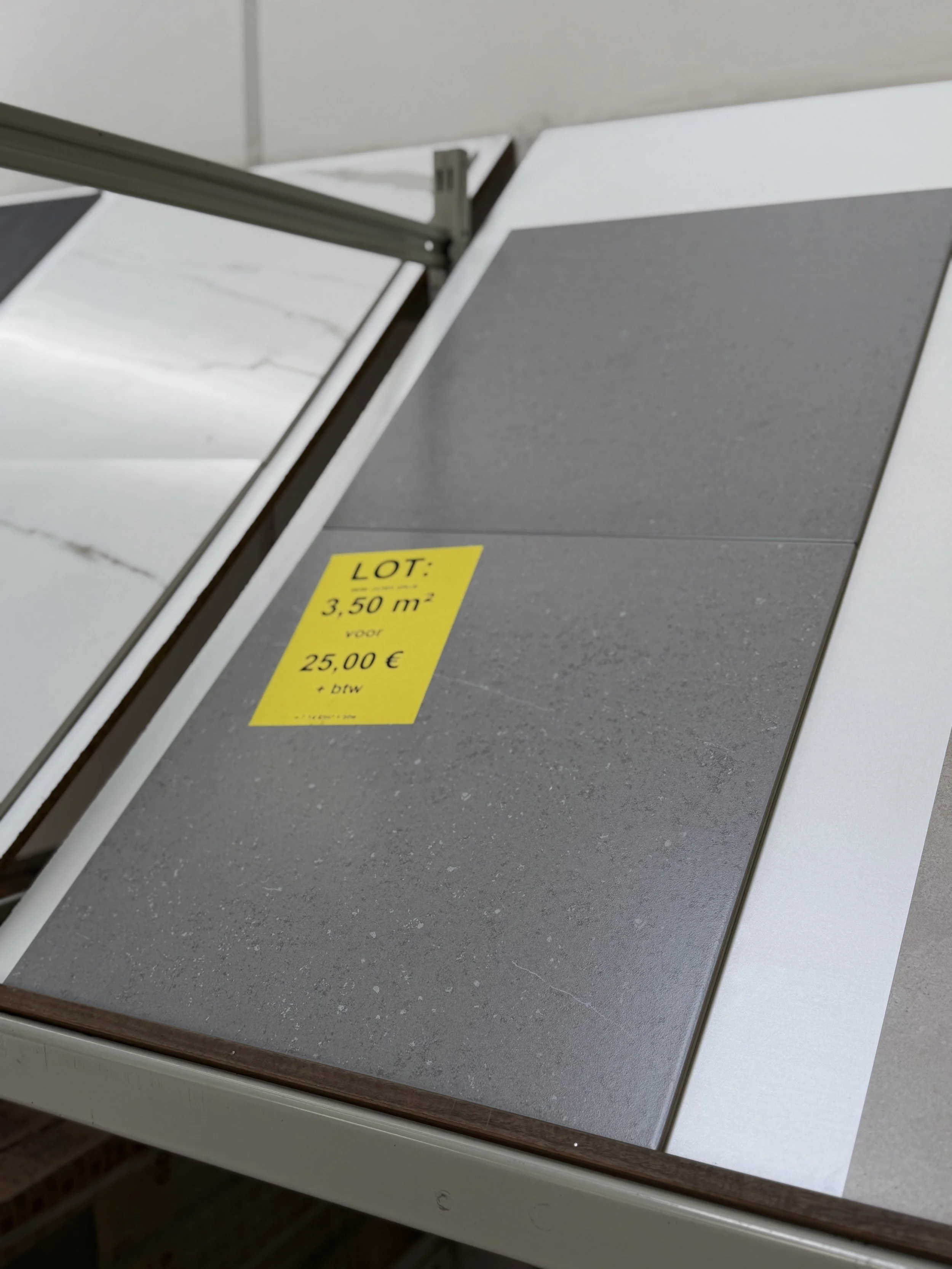 Twee stalen platen, een witte met een marmerpatroon en een grijze, liggen naast elkaar, met een gele prijskaart die 3,50 m² en 25,00 € vermeldt.