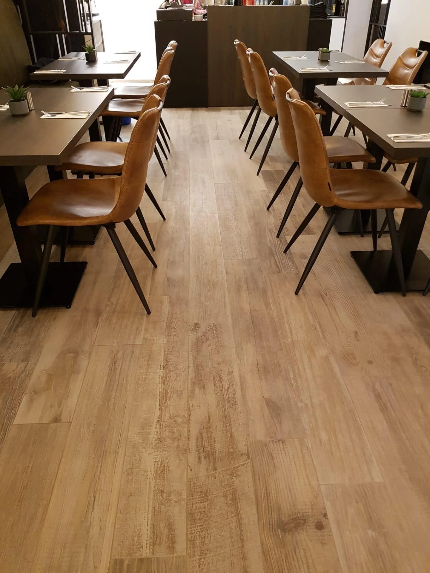 Een restaurant met meerdere houten tafels en leren stoelen, decoraties en planten op de tafels, en een bar of service counter op de achtergrond.