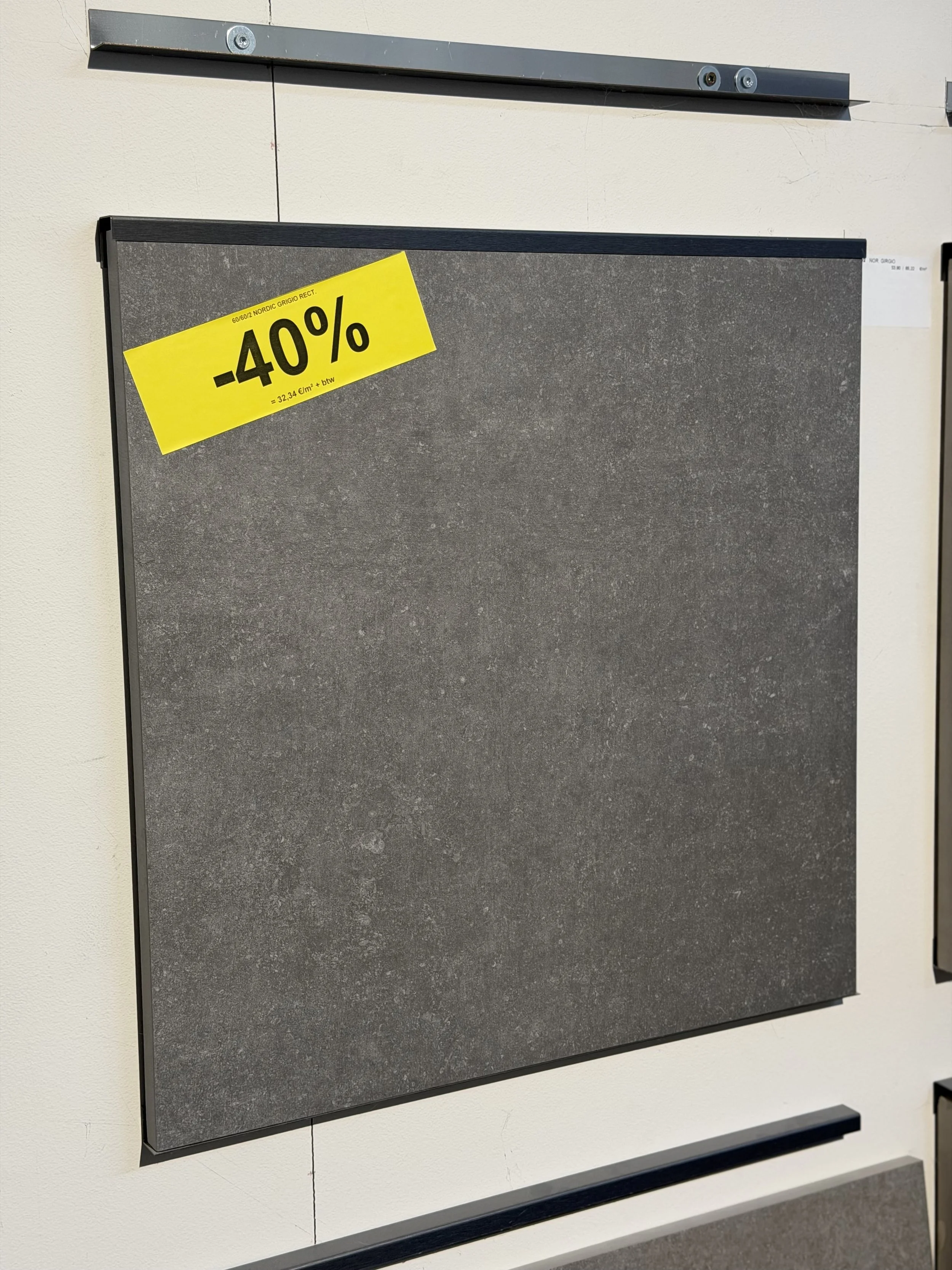 Een grijs zwartachtig bord met een grote gele aanbiedingsticker die 40% korting aangeeft en een witte muur erachter.