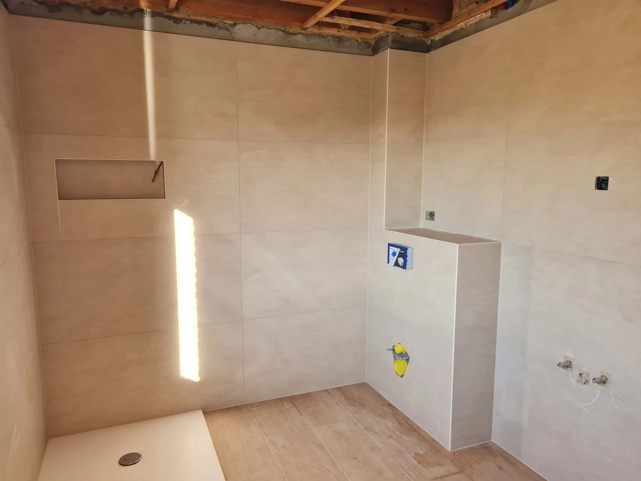 Ongeïnstalleerde badkamer met beige wandtegels, open elektrische aansluitingen en geen sanitair.