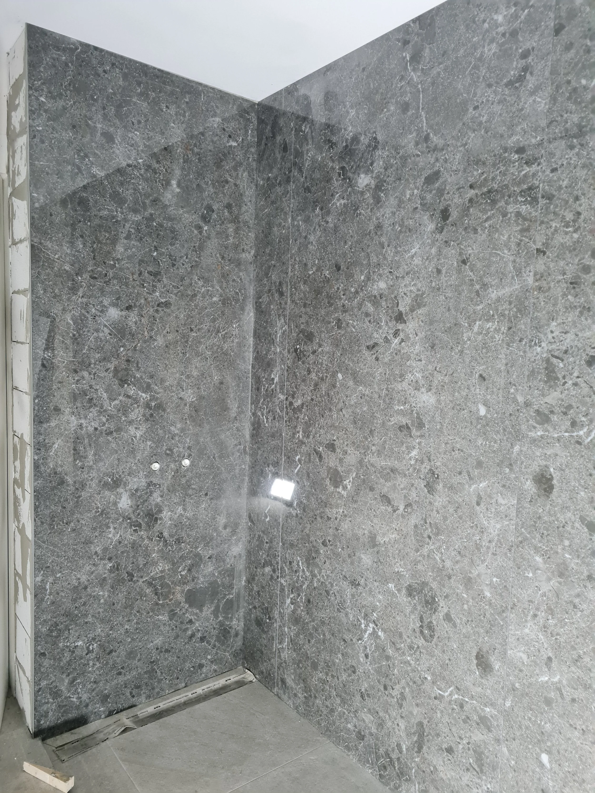 Grote grijze marmeren tegels op een rustige muur, nog niet afgewerkt, in een badkamer of modern interieur.