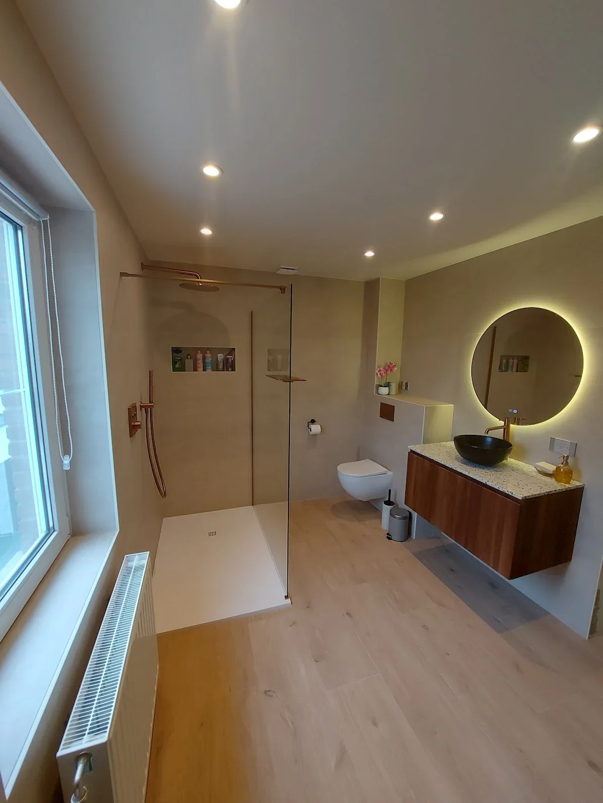 Moderne badkamer met inloopdouche, wandtoilet, houten kast met wastafel en ronde spiegel met verlichting