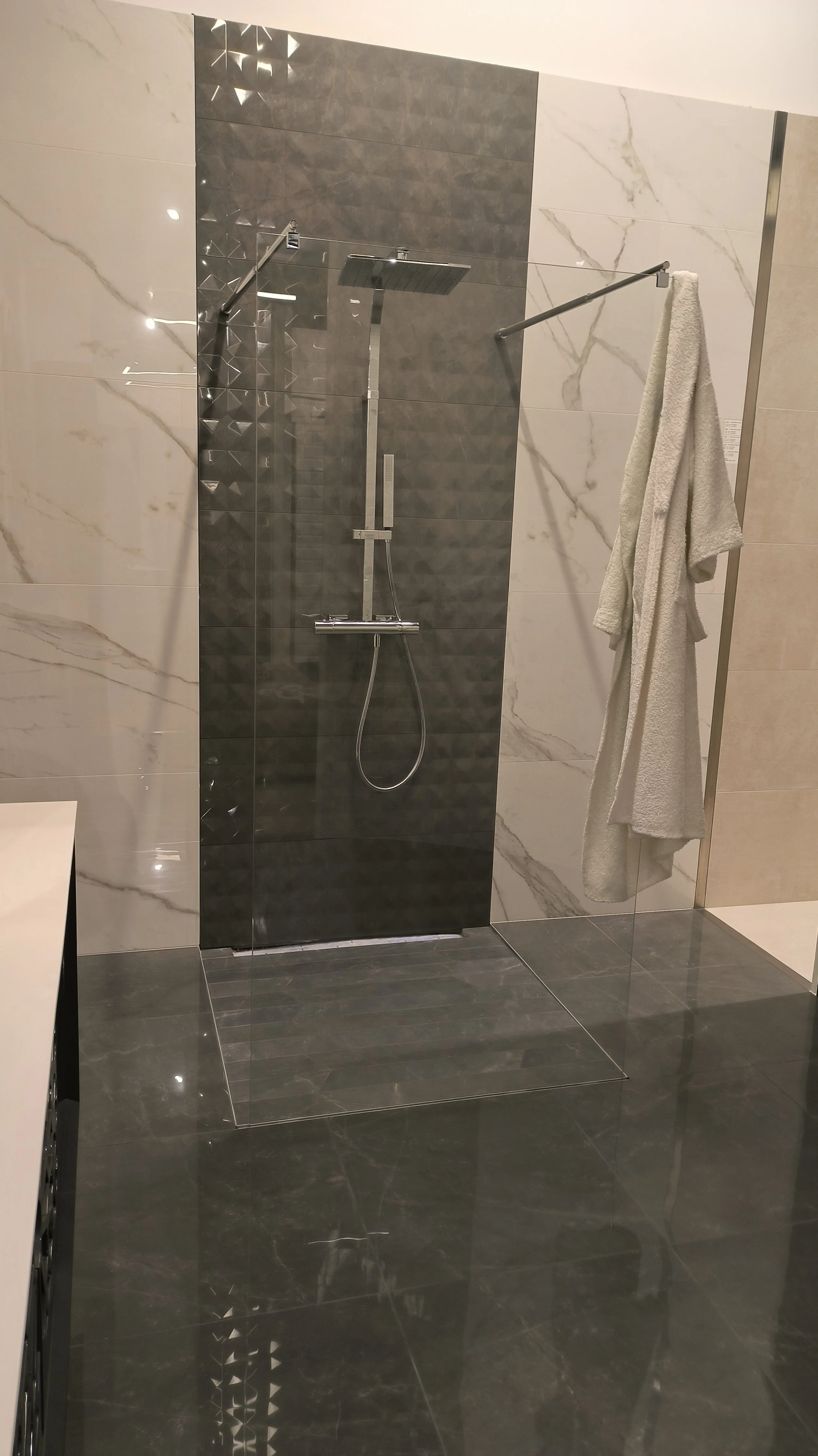 Een moderne douchecabine met een regen-douchekop, een verstelbare handdouche, en een houten handdoekrek met een witte handdoek.