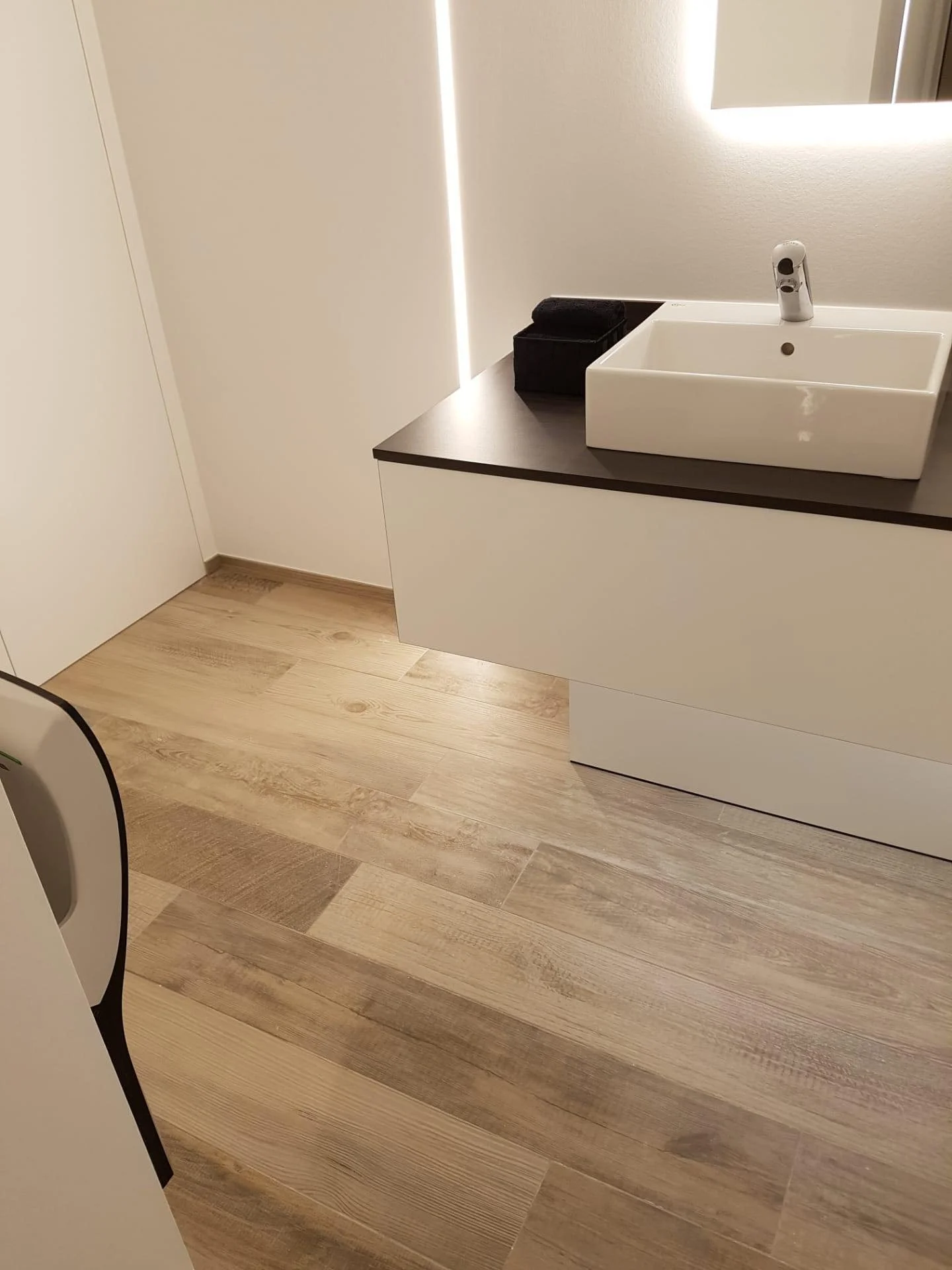 Moderne badkamer met wasbak, spiegel met verlichting, en houten vloer.