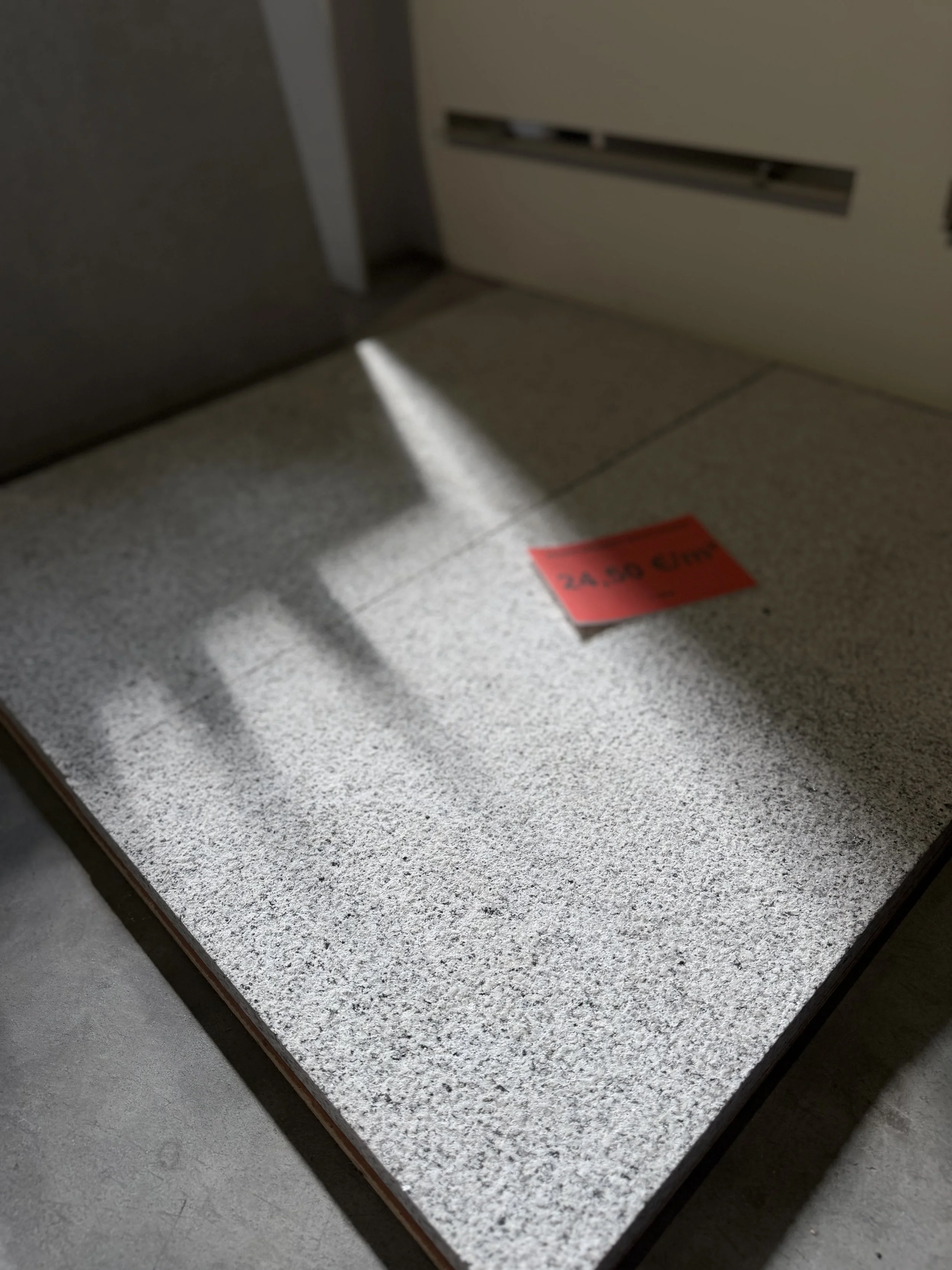 Een deur met een kleine uitsparing, waarvan een stukje licht doorheen schijnt, en een rode strip op de vloer met tekst. De vloer is grijs en het is een goed verlichte ruimte.