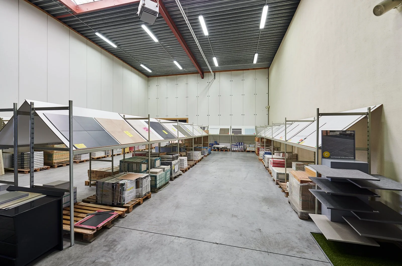 Interieur van een groothandel of meubelwinkel met planken vol tegels en vloerbedekkingen, lege vloer en hoge plafonds.