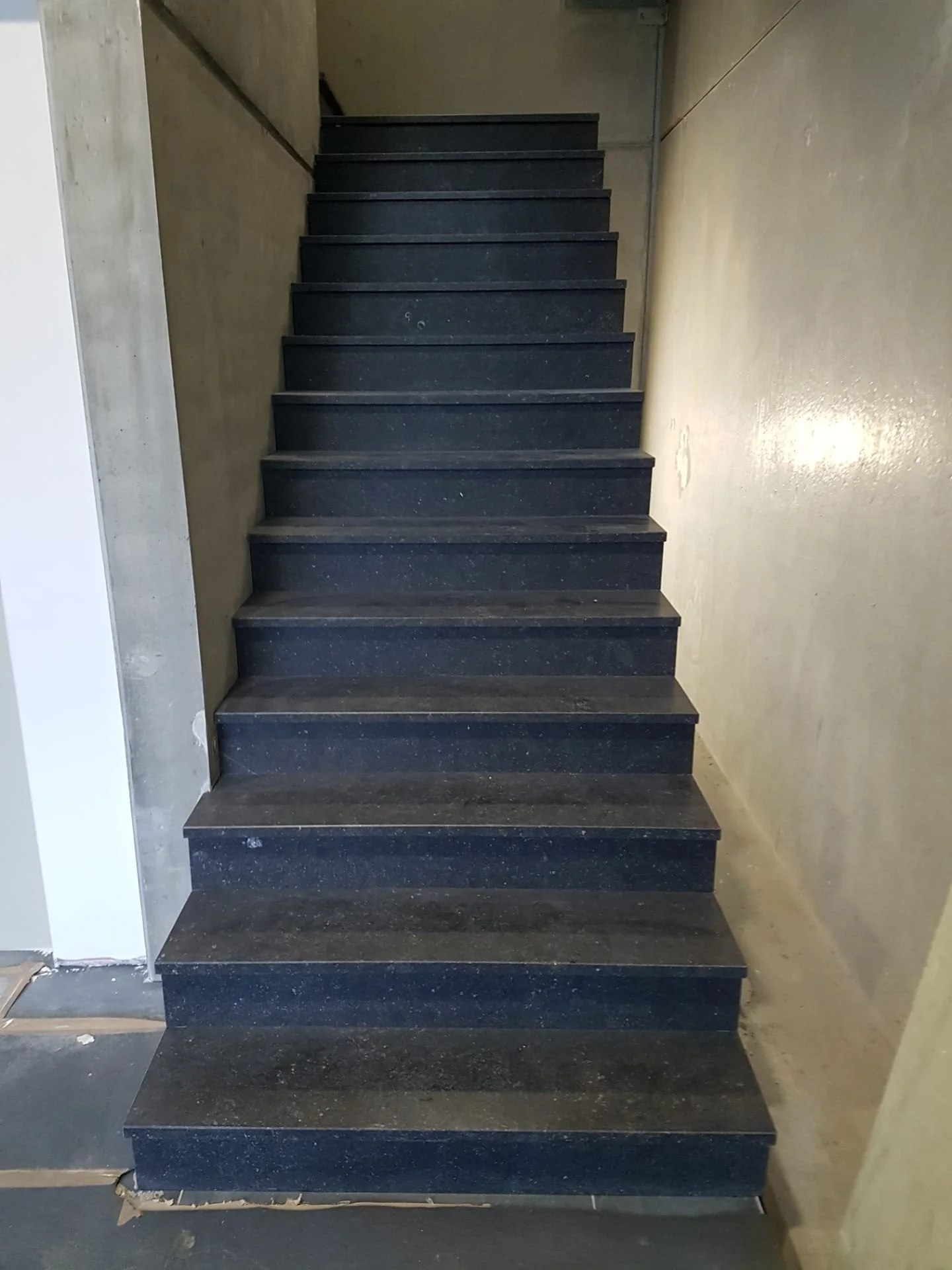 Trap met zwarte treden in een divers bouwproject, op een betonnen vloer en muren.
