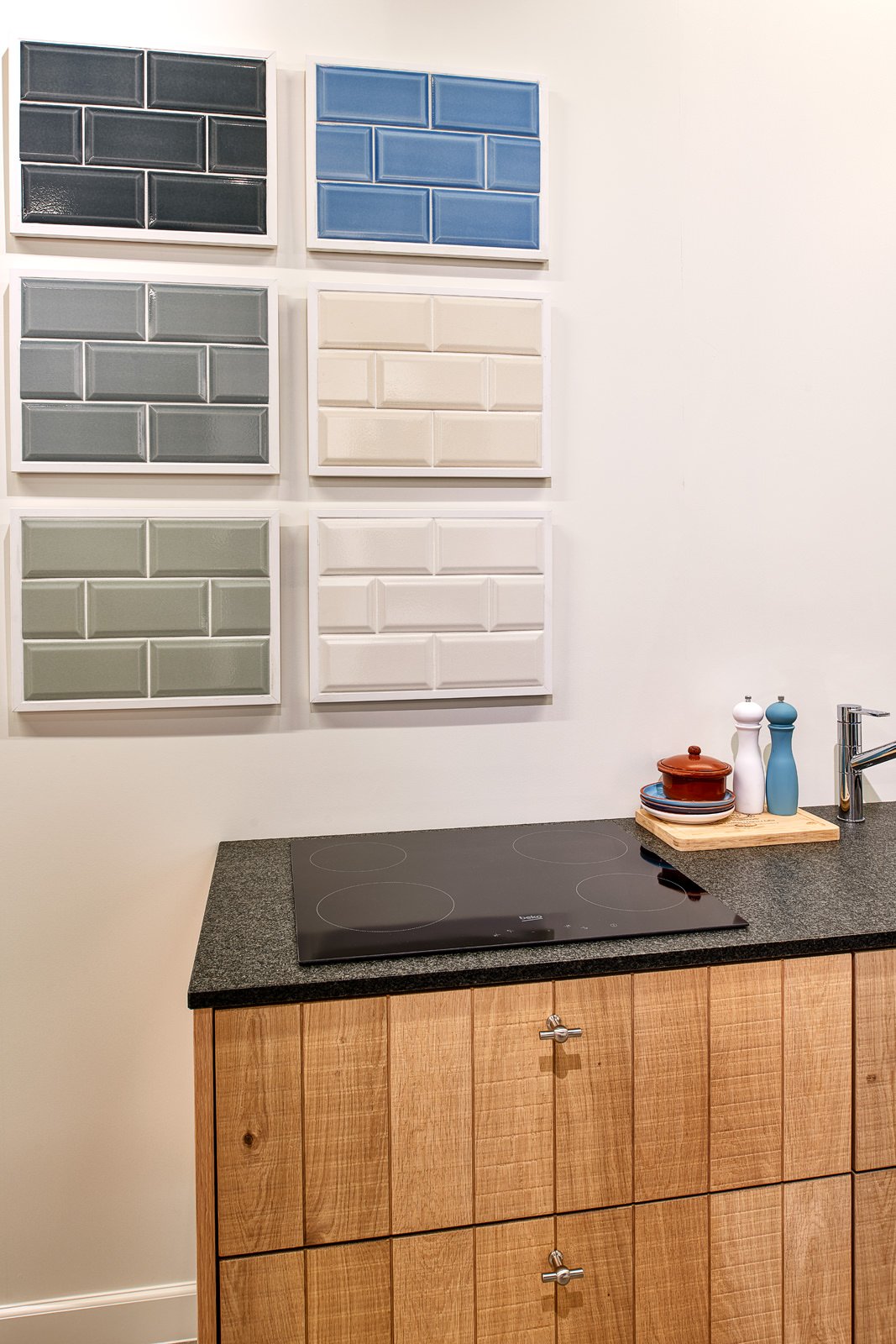 Elke muur heeft vier verschillende tegels, in blauw, grijs, groen en wit, in een keuken met houten kasten en een zwart kookplaat.